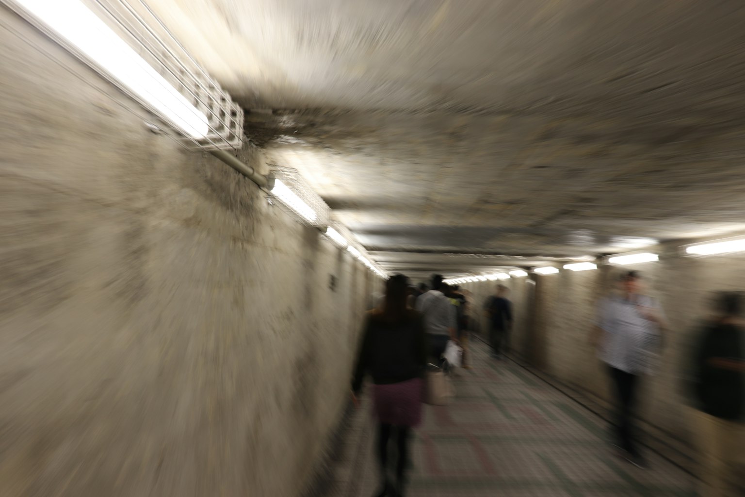 Image floue de personnes marchant dans un passage souterrain Murs en béton éclairés par des lumières fluorescentes brillantes