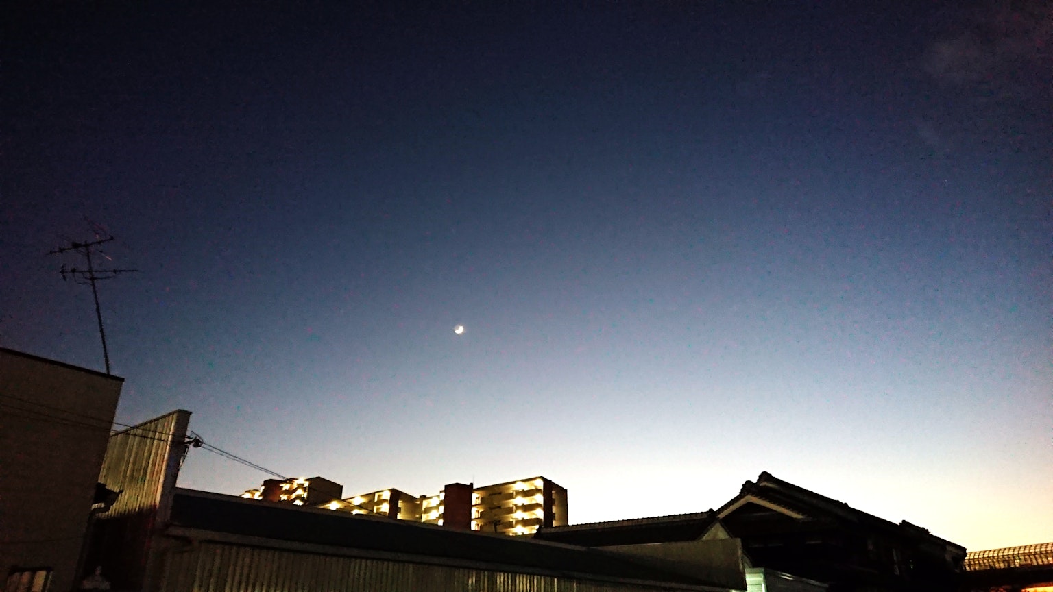 Moon in the twilight sky with silhouettes of nearby buildings