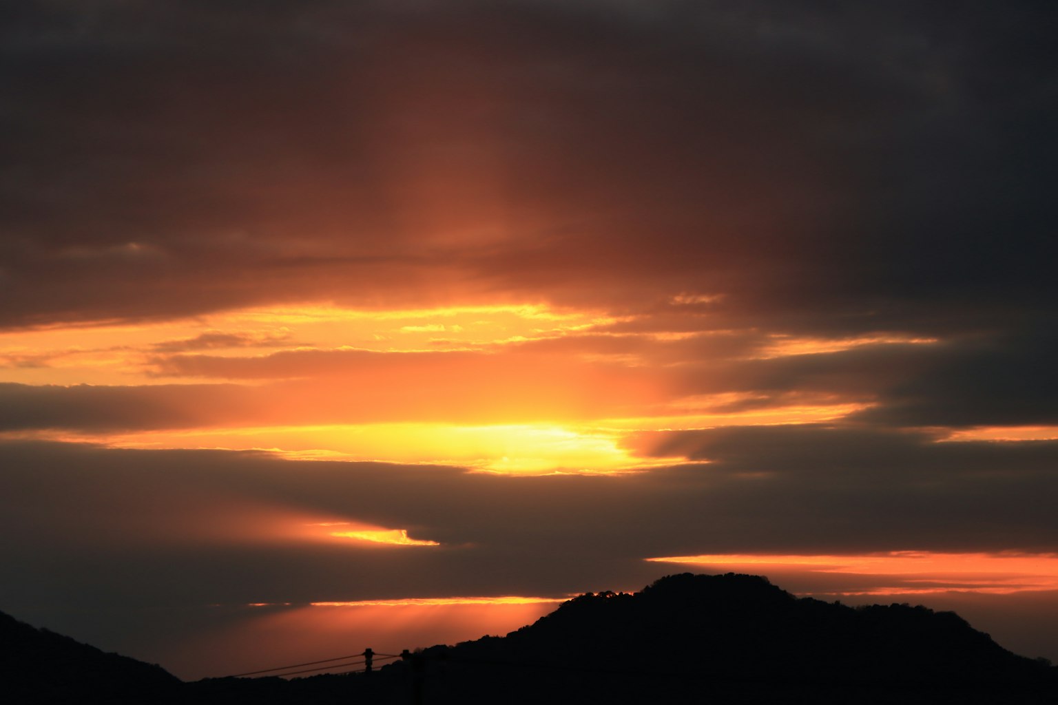 Langit senja dengan awan oranye dan ungu di atas bukit jauh