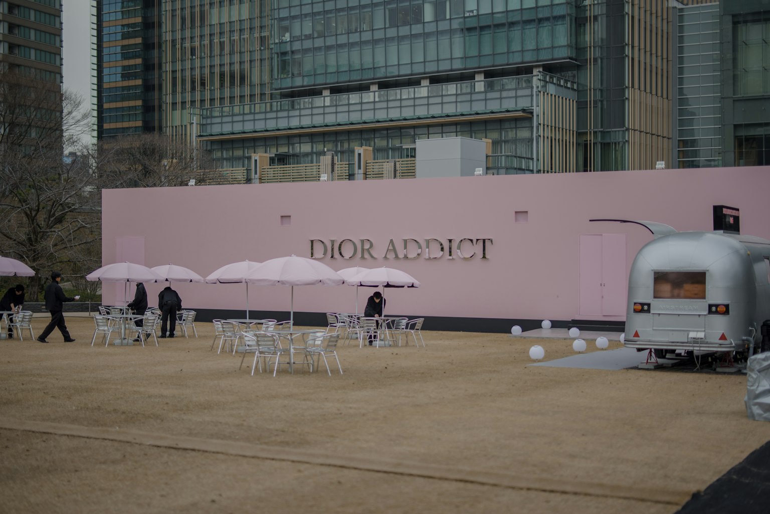 Espacio exterior con una pared rosa que dice 'DIOR ADDICT' y mesas con sombrillas