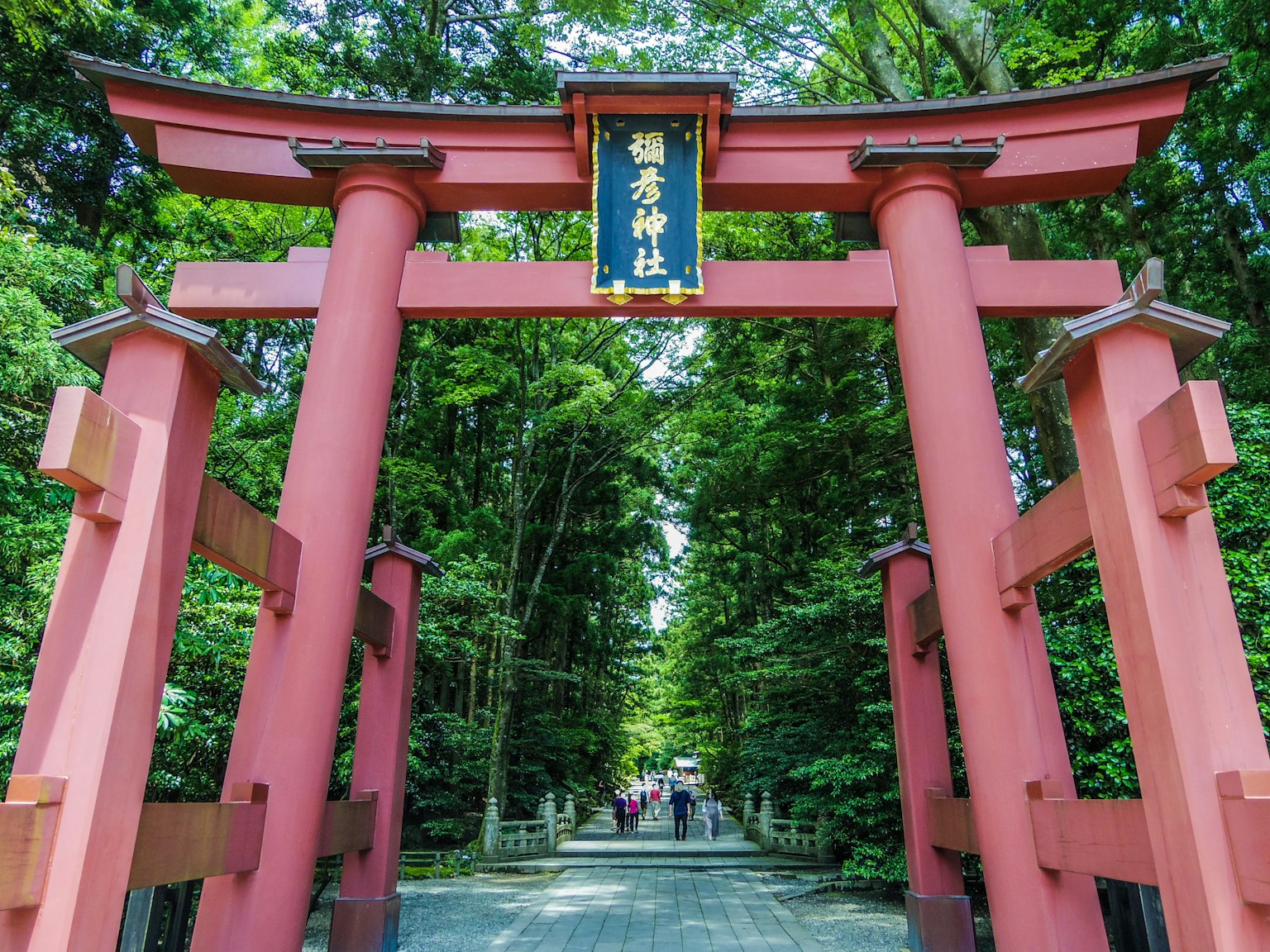 Ingresso di un cancello torii rosso circondato da vegetazione con un'insegna del santuario