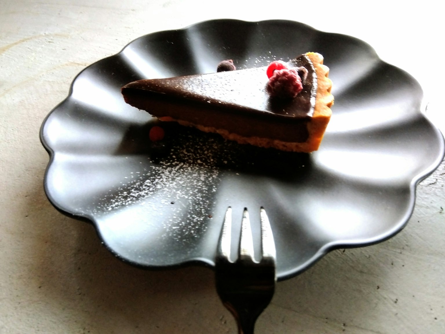 A slice of chocolate tart on a black plate with a fork