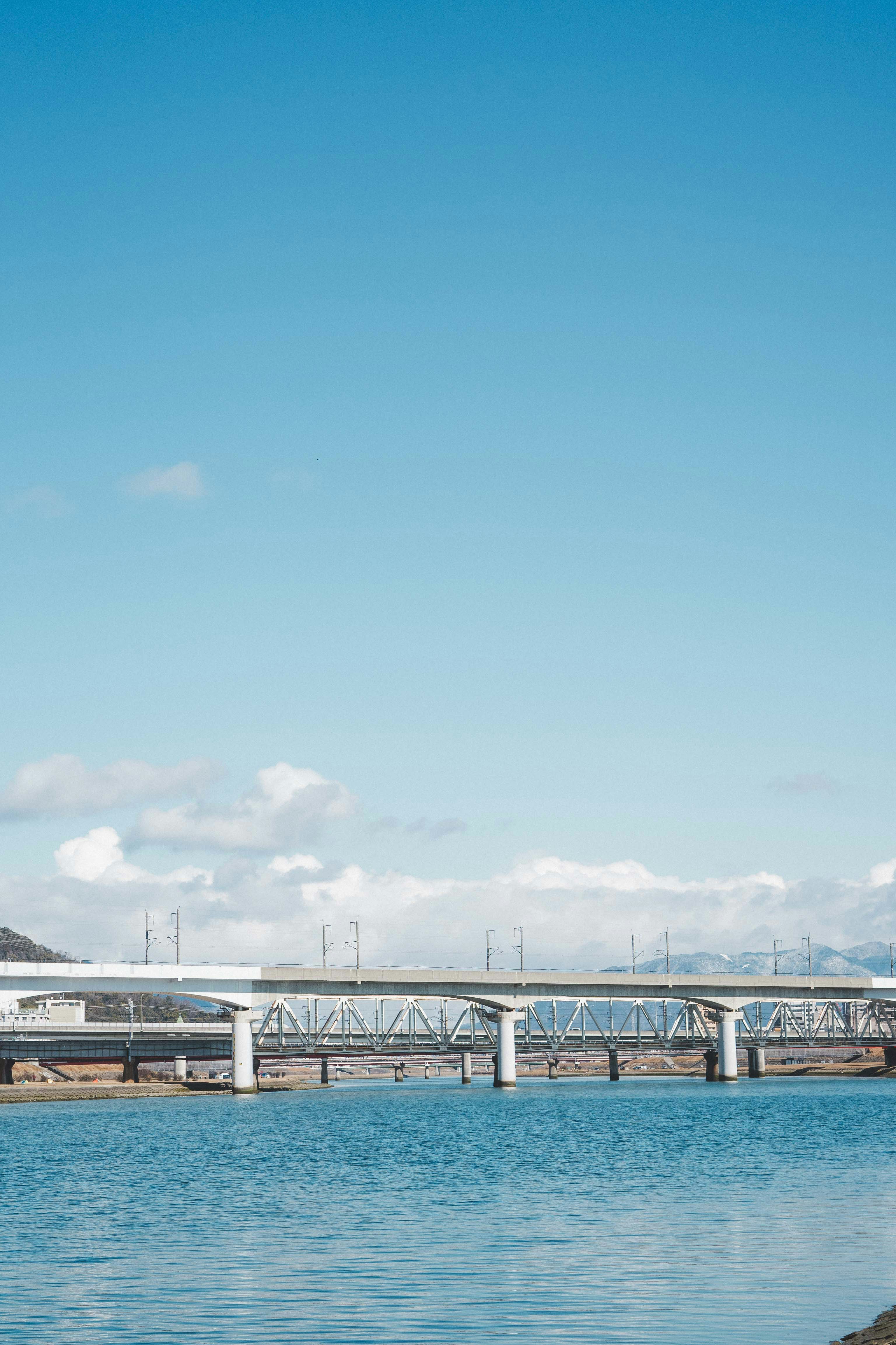 青い川面と橋が見える河川敷の景色