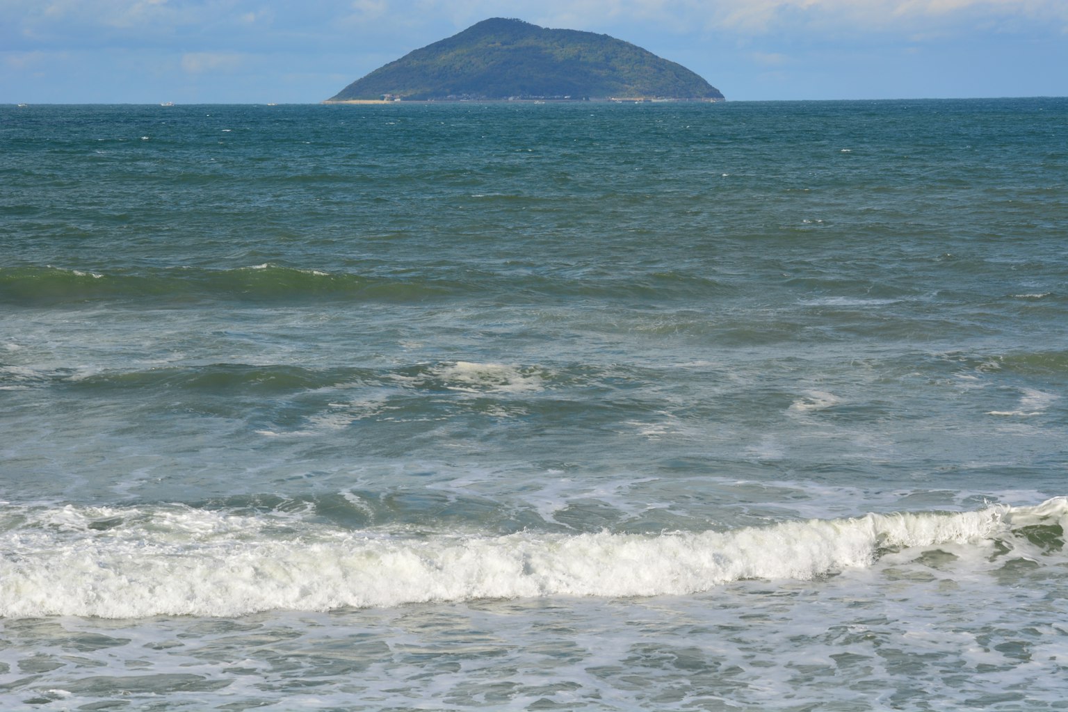 Scenic view of blue ocean waves crashing on a beach with a small island in the distance