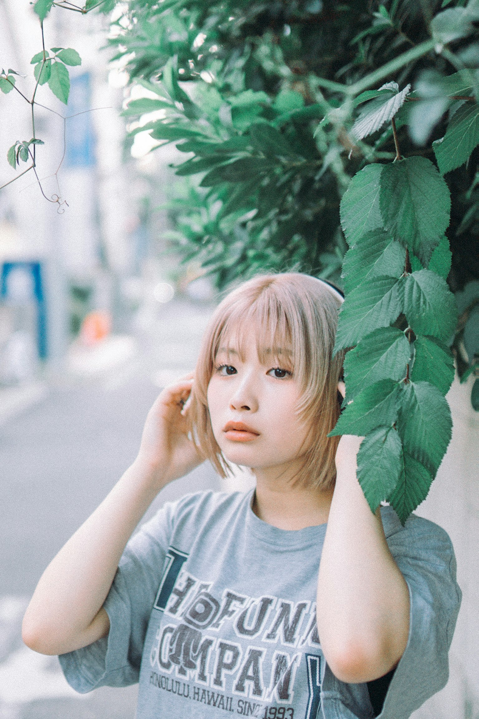 A woman surrounded by greenery in the city wearing headphones