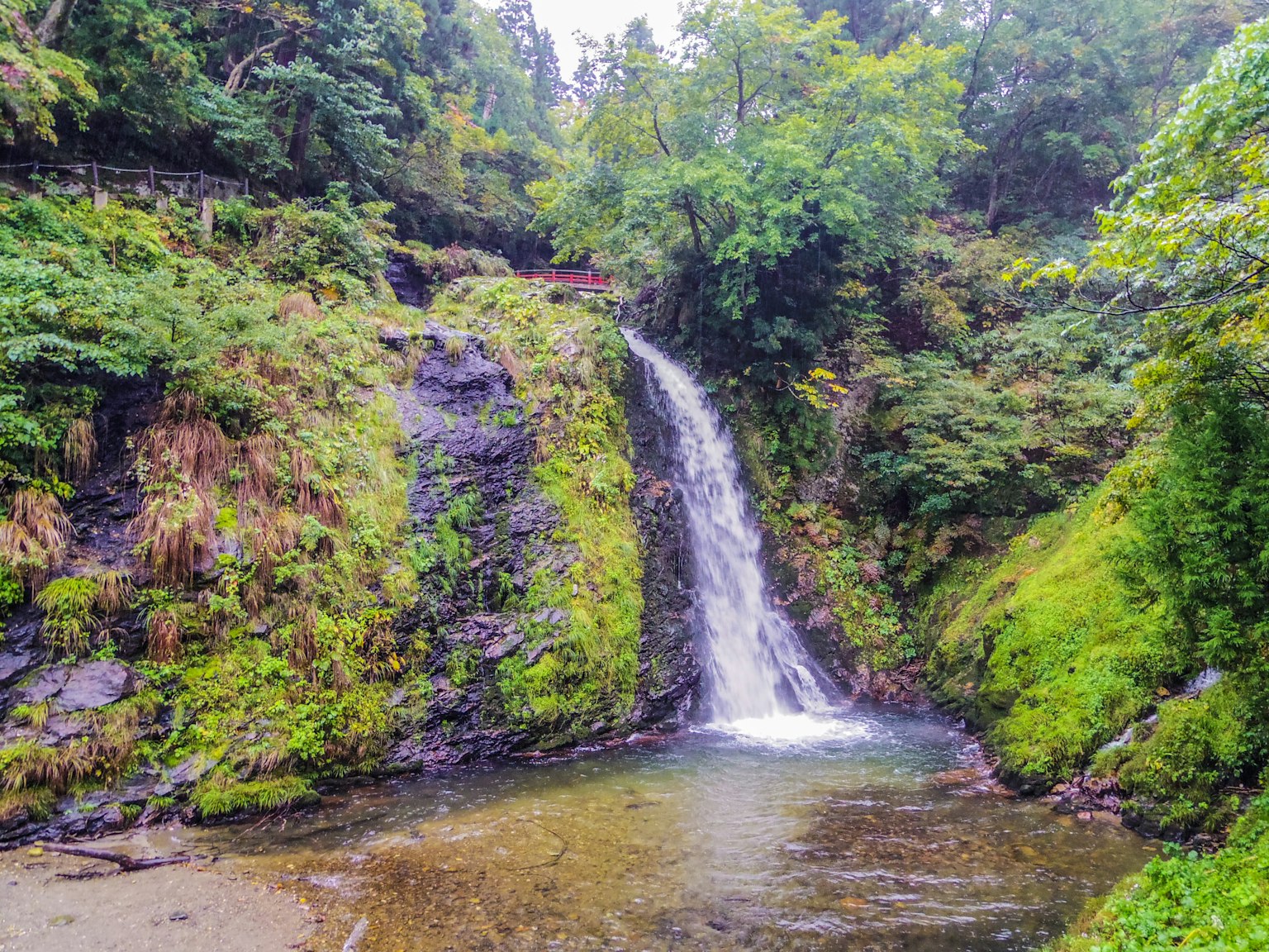 Sebuah air terjun kecil yang dikelilingi oleh pepohonan subur dan air tenang