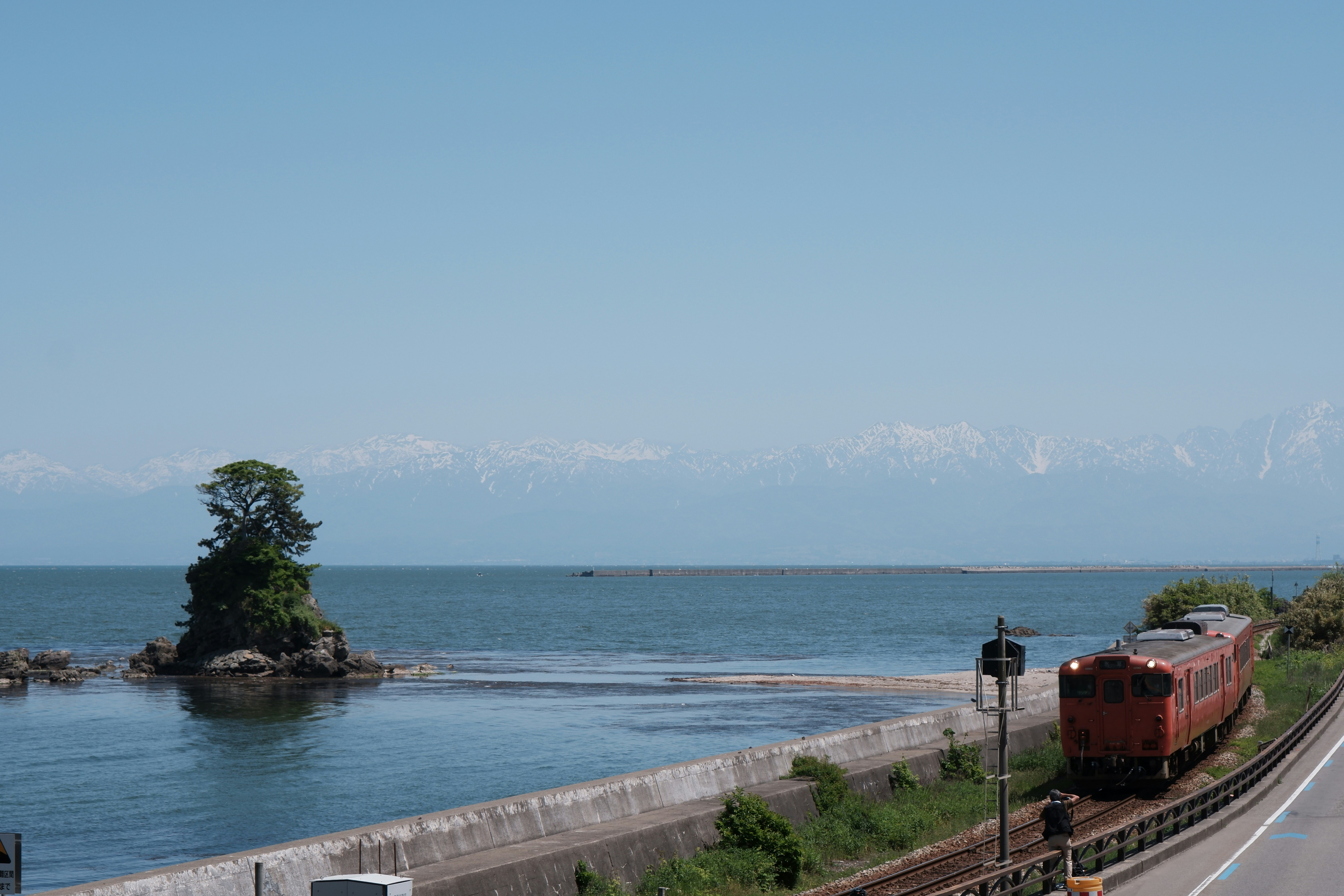 海辺を走る赤い列車と小さな島の風景