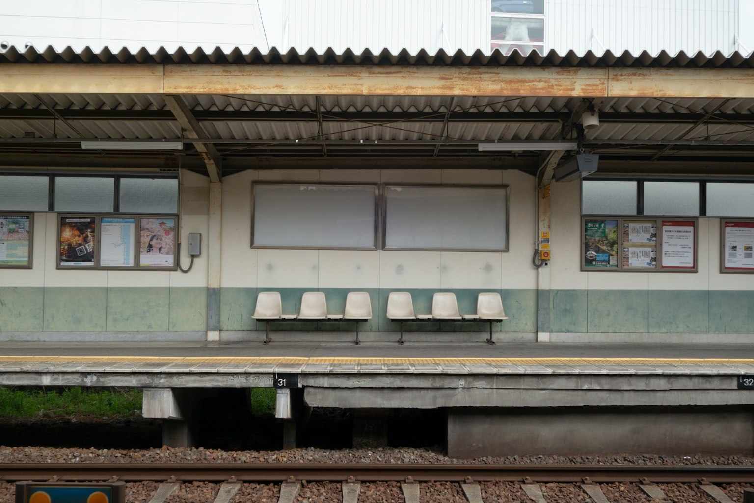 Bancos blancos alineados en una plataforma de tren con carteles en la pared