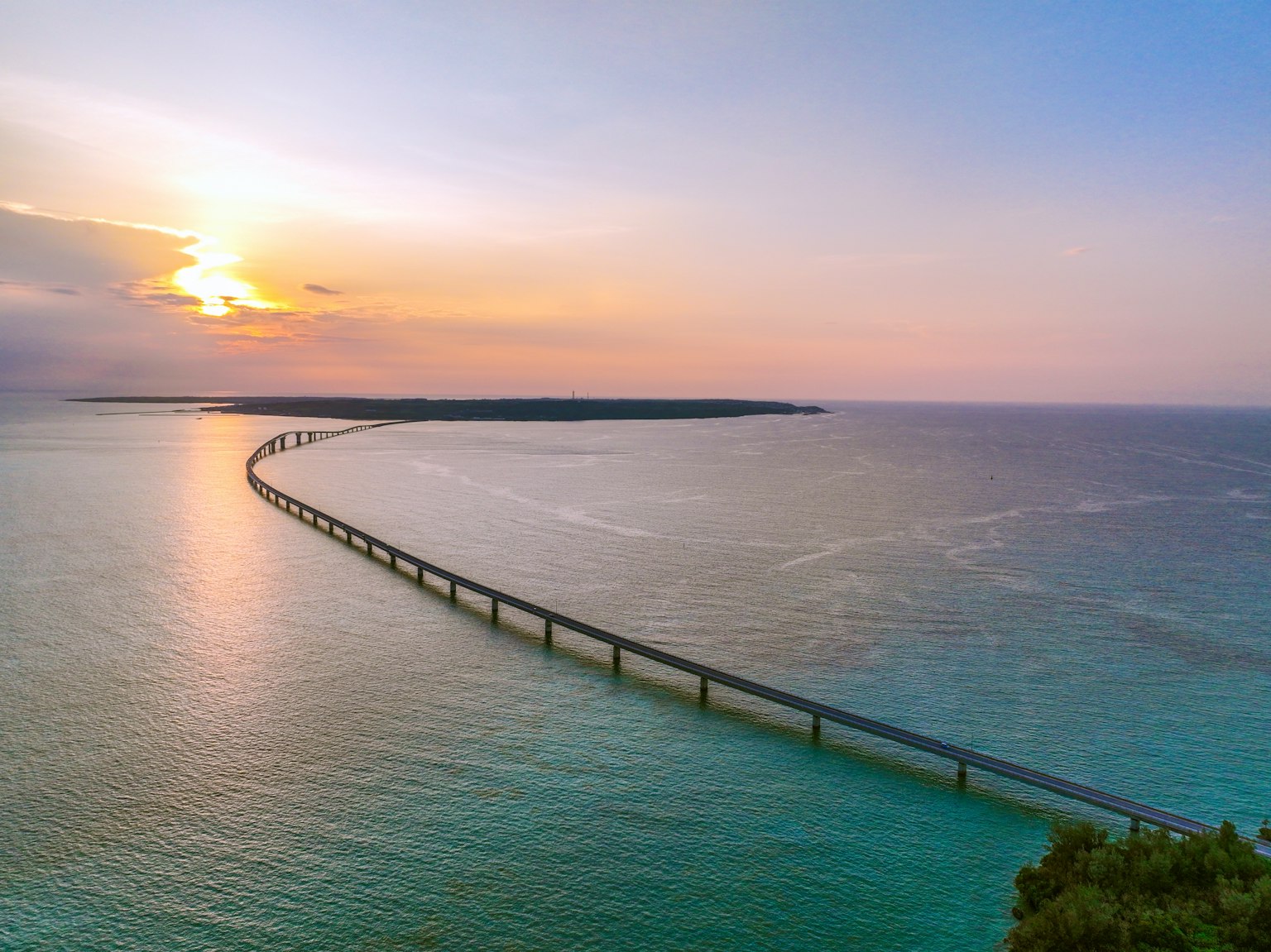 Un lungo ponte sopra un'acqua blu con un tramonto sullo sfondo