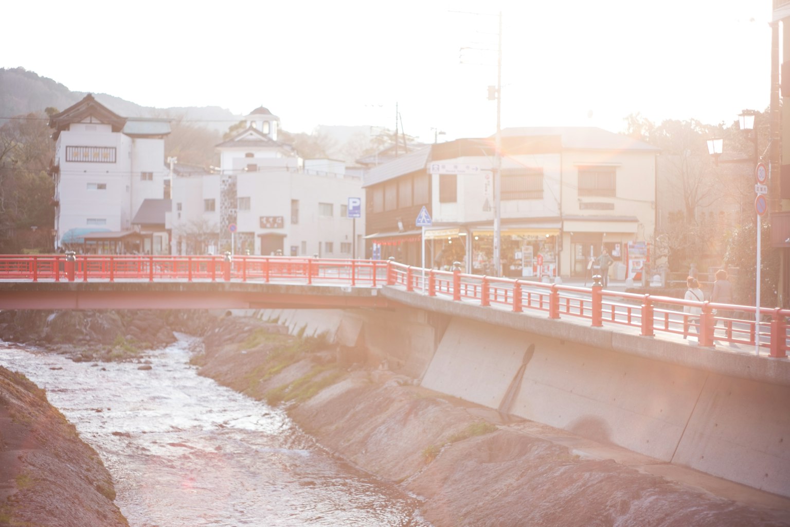 一座红色桥梁横跨河流，附近建筑在柔和的阳光下