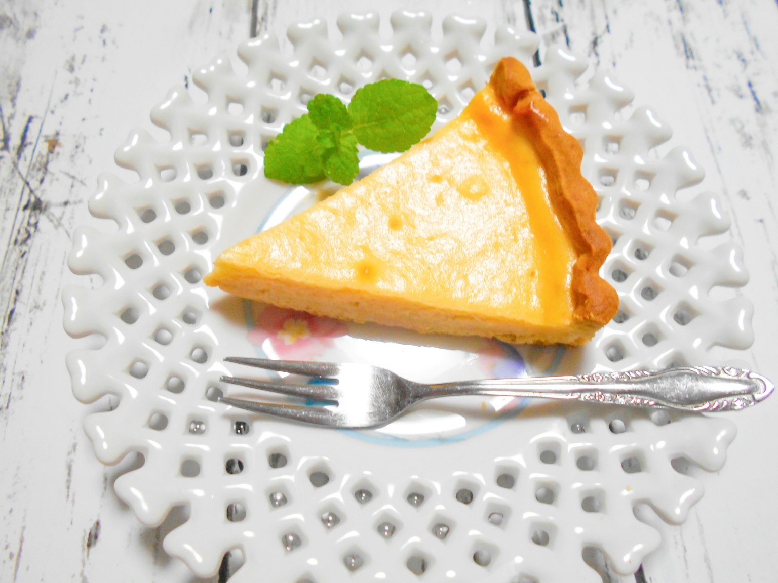 Une tranche de tarte au citron sur une assiette blanche décorative avec une feuille de menthe
