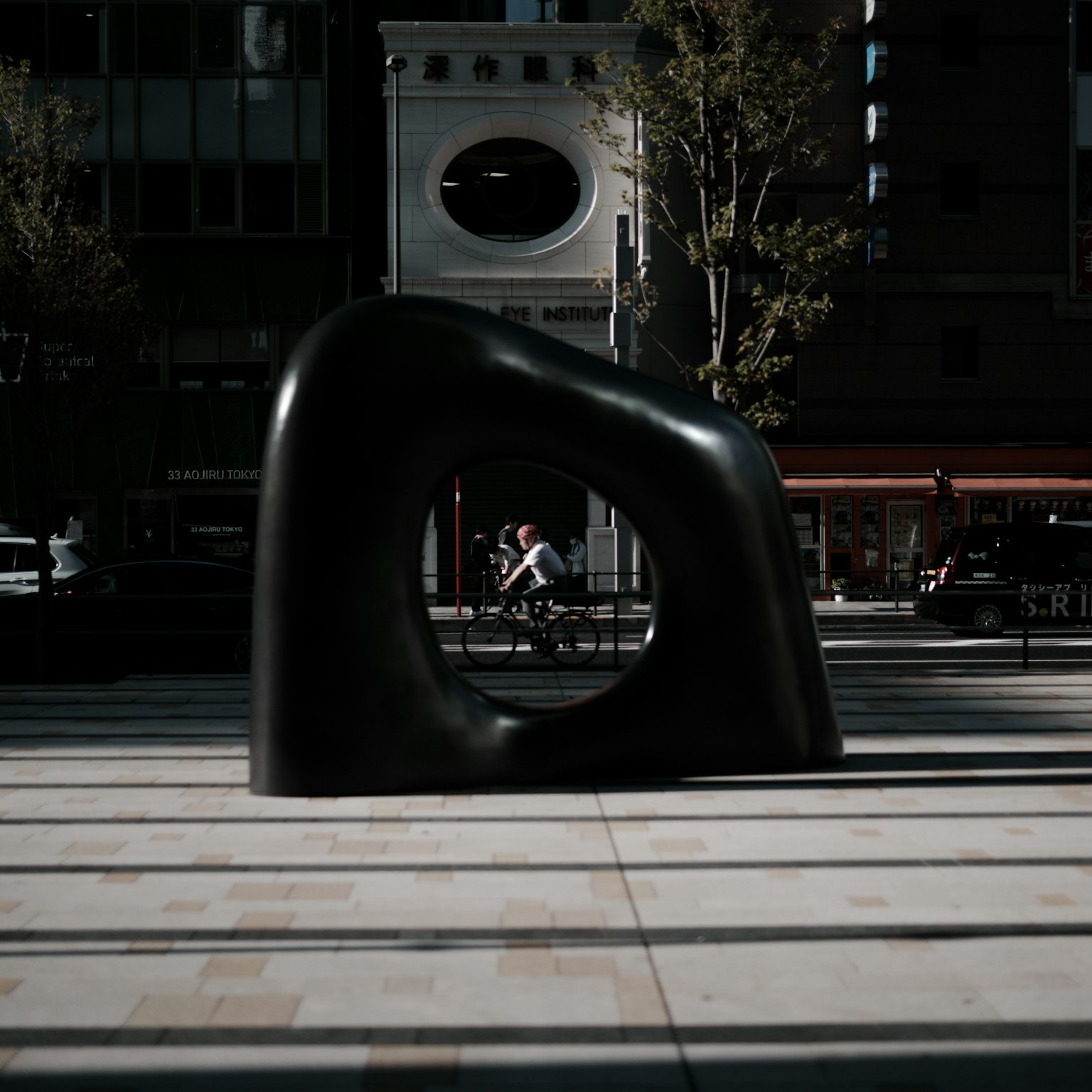 Escultura negra abstracta en una plaza con fondo urbano