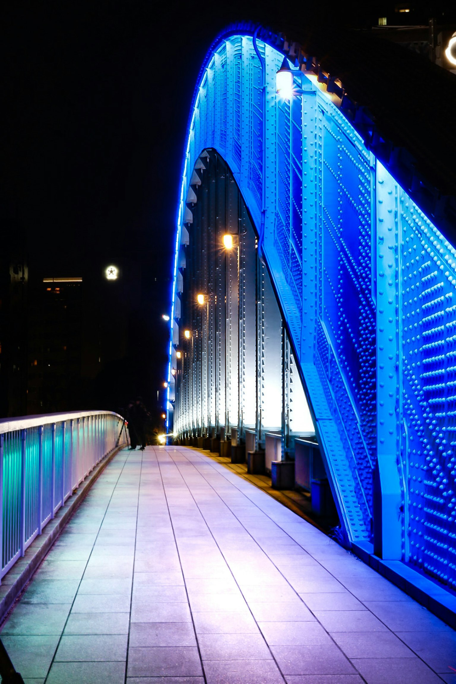 สะพานโค้งสีน้ำเงินที่มีแสงสว่างในตอนกลางคืนพร้อมทางเดิน