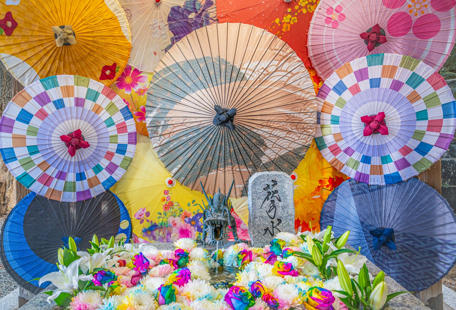 Ombrelli giapponesi colorati disposti dietro una decorazione floreale con una statua