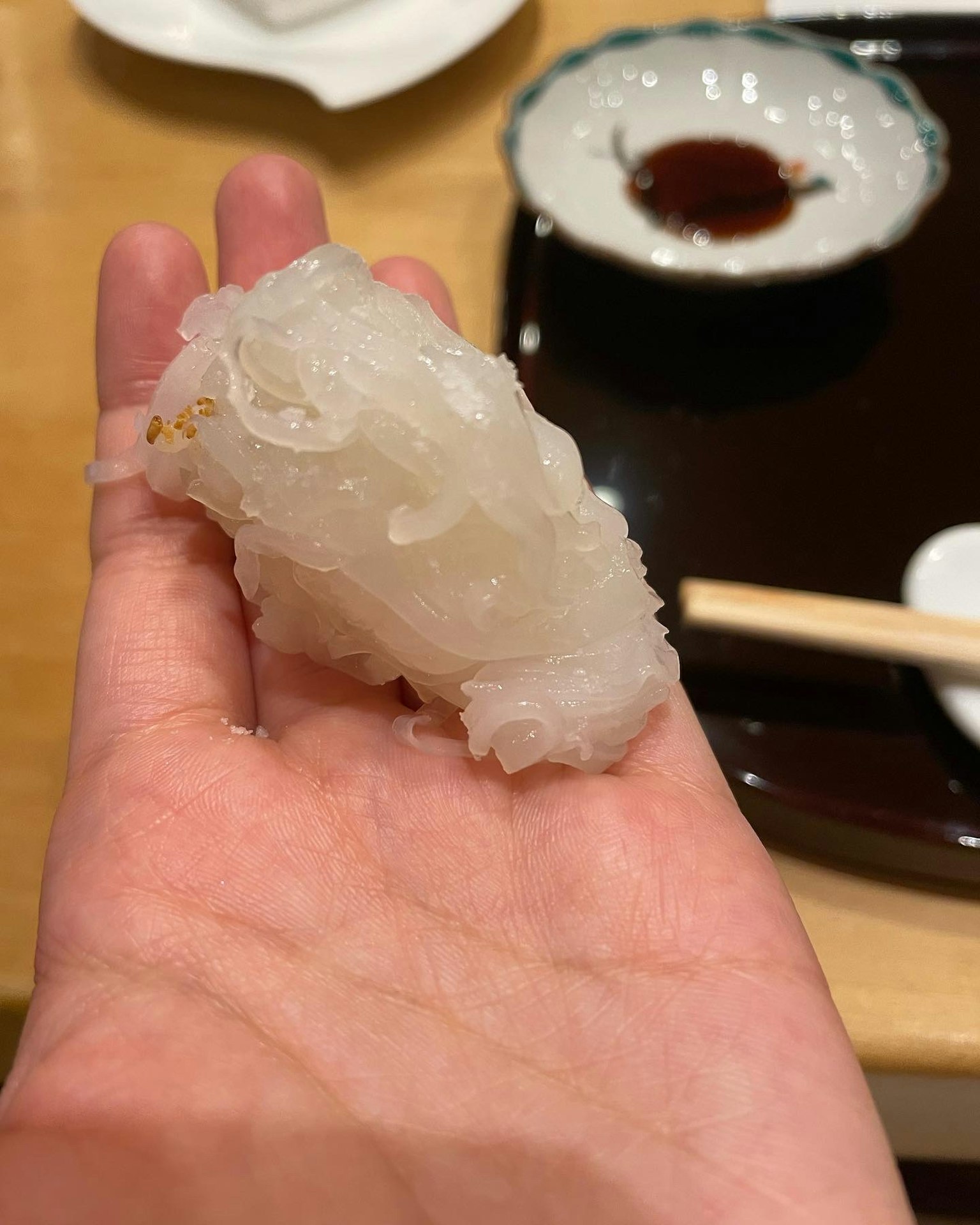 Un alimento translúcido descansando en una mano con un pequeño plato de salsa de soja al fondo
