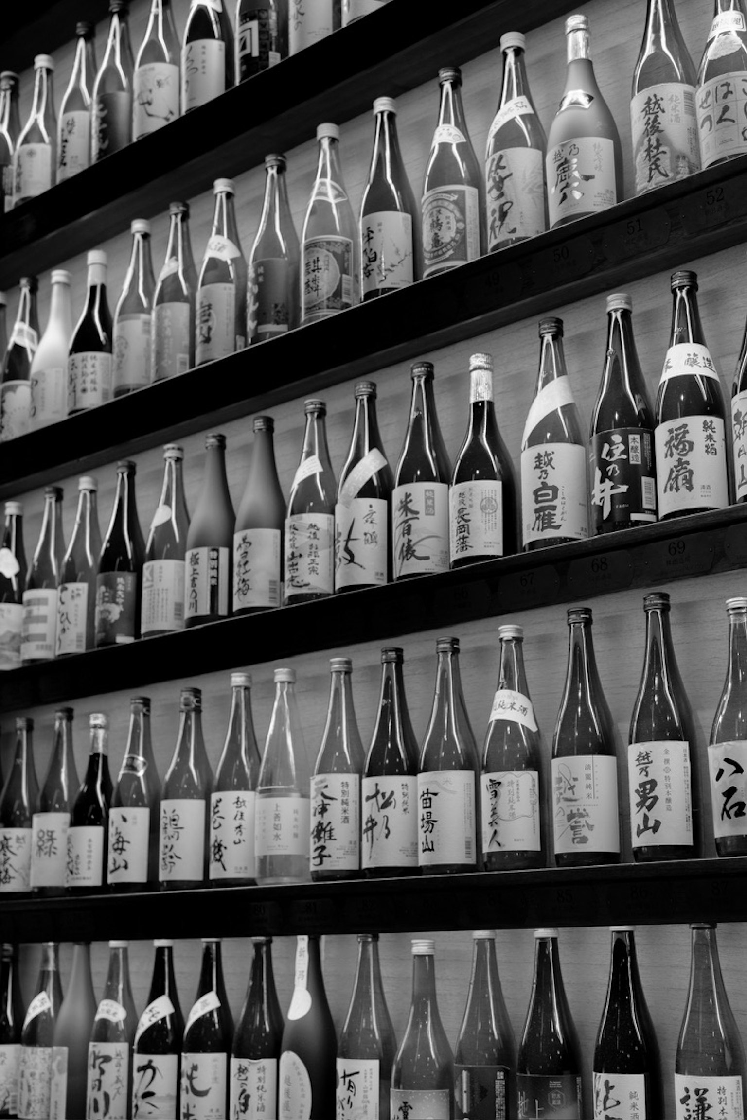 Affichage de bouteilles de saké en noir et blanc disposées sur un mur