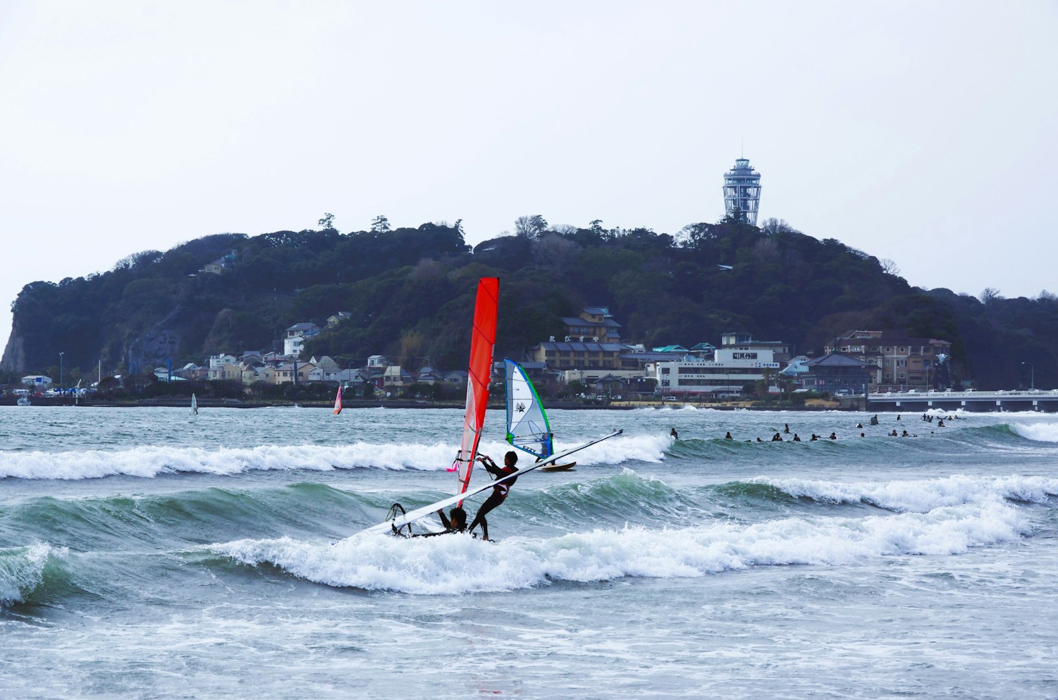 Una persona practicando windsurf en el océano con un faro al fondo