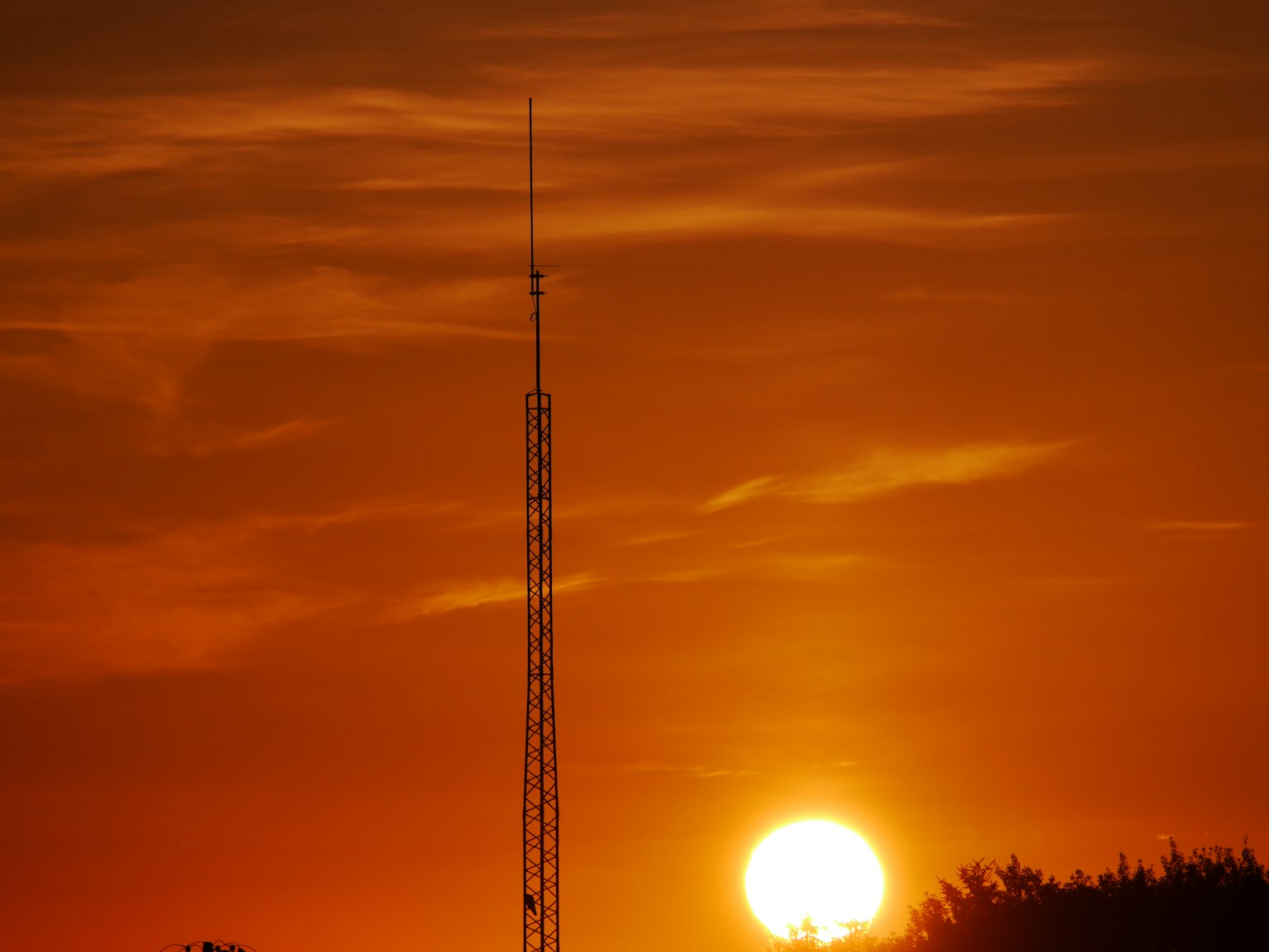 Silueta de una torre de comunicación contra un vibrante atardecer naranja