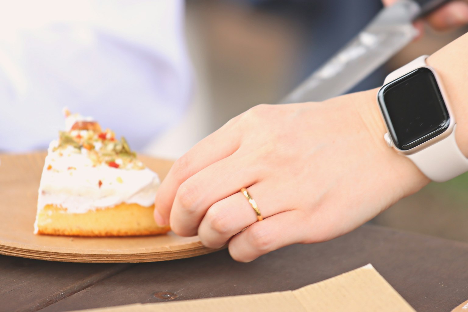 A hand holding a slice of cake with a smartwatch on the wrist