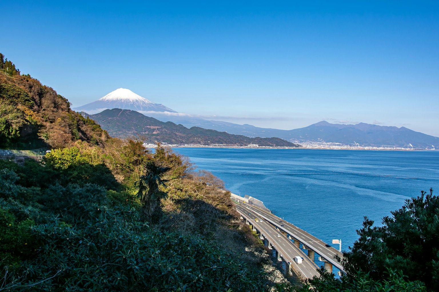 Scenic view of Mount Fuji and the ocean with green hills and clear blue sky
