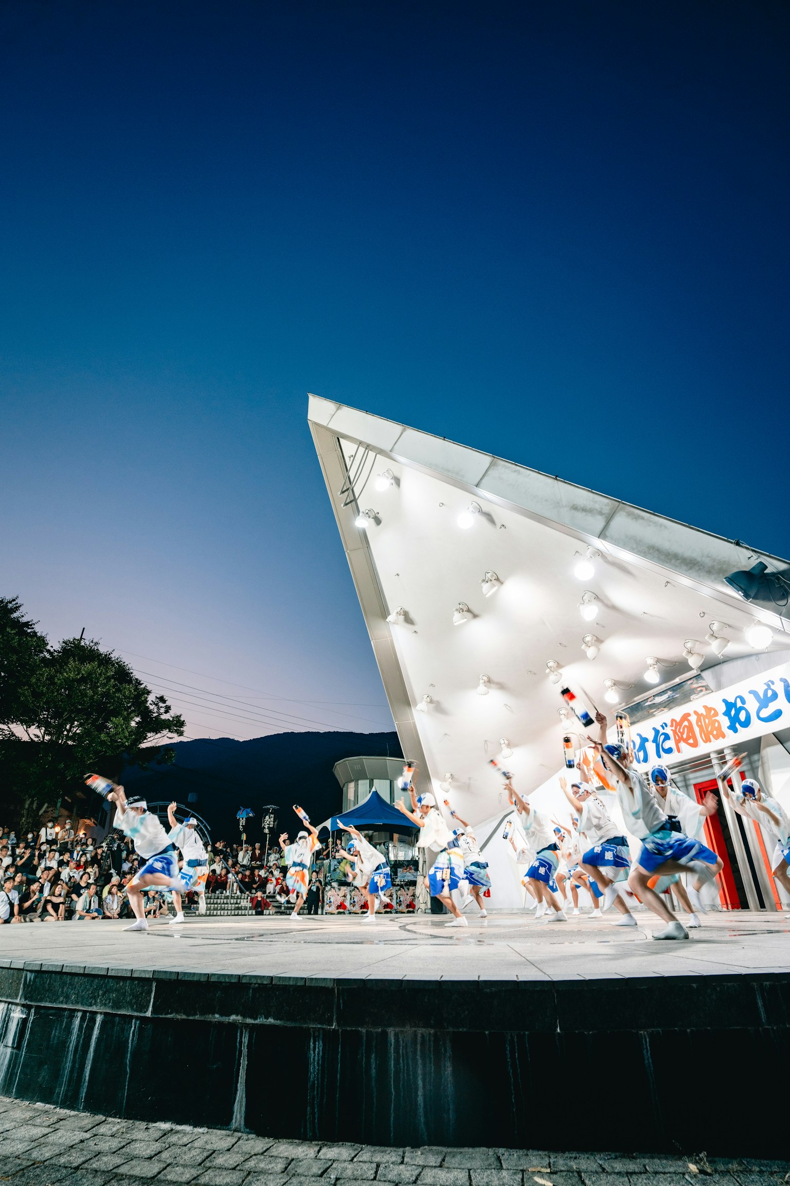 People dancing under a blue sky with a modern architectural stage