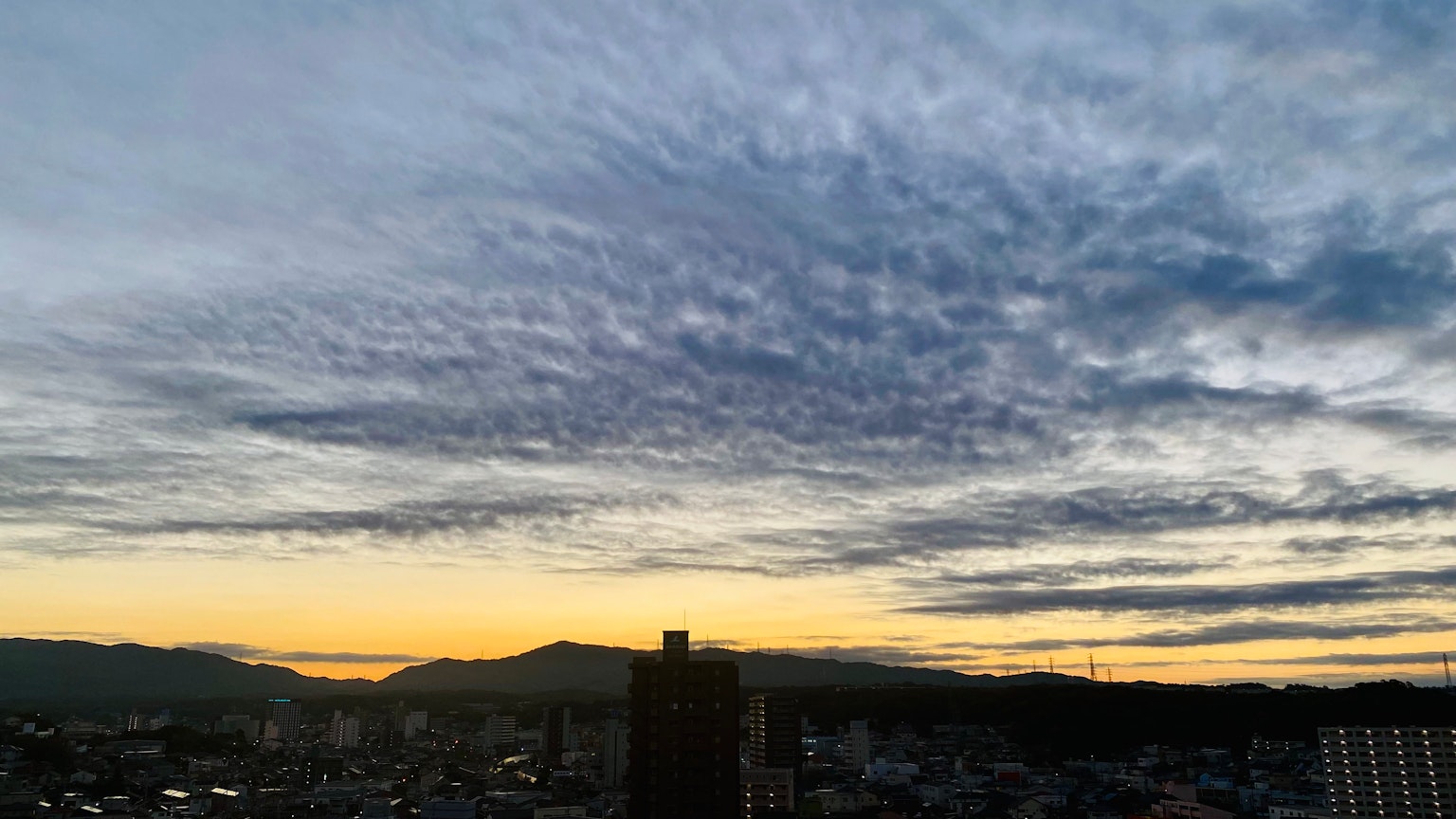 Langit saat matahari terbenam dengan awan dan pegunungan terlihat bangunan di bawah