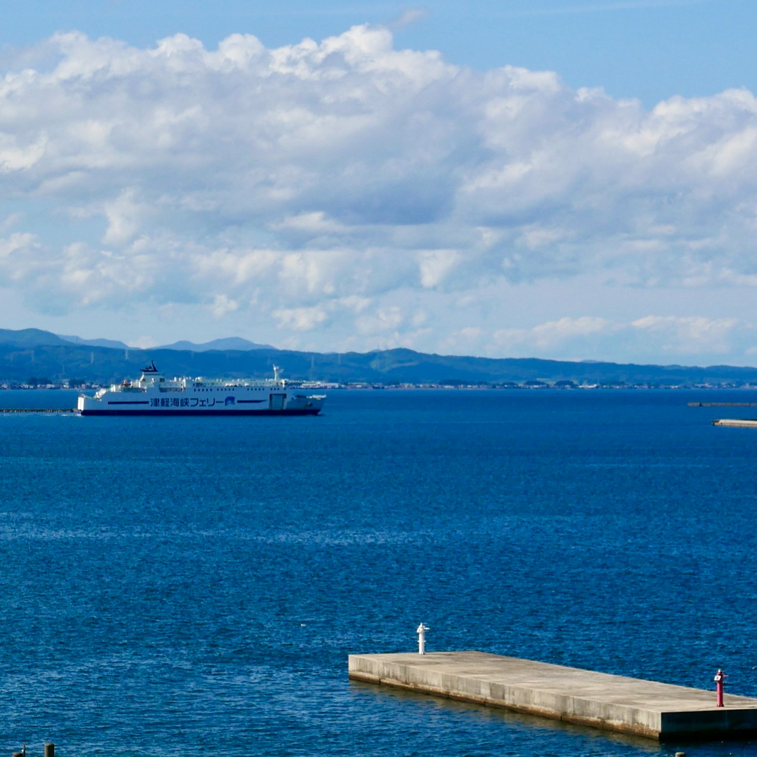 View of a harbor with a ship on blue water and distant mountains