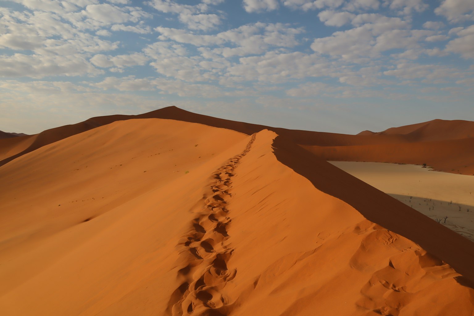 Dunes de sable orange s'étendant sous un ciel bleu avec des nuages