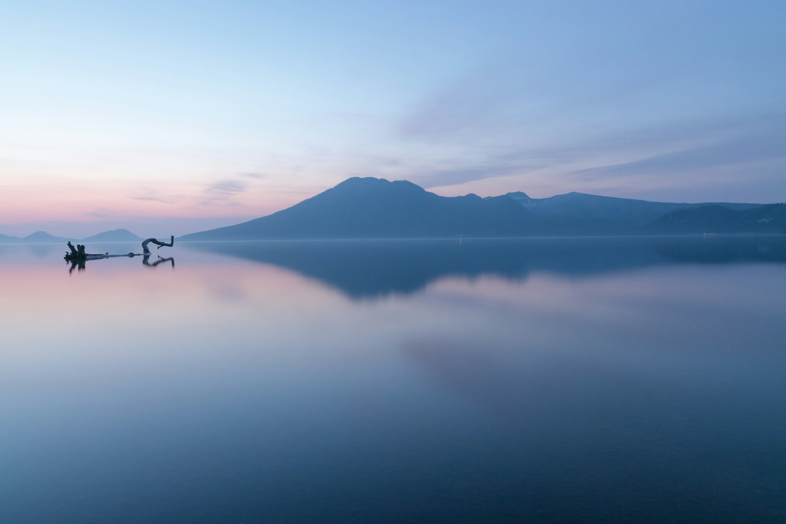 Paisaje montañoso sereno reflejado en la superficie tranquila del lago colores suaves del amanecer