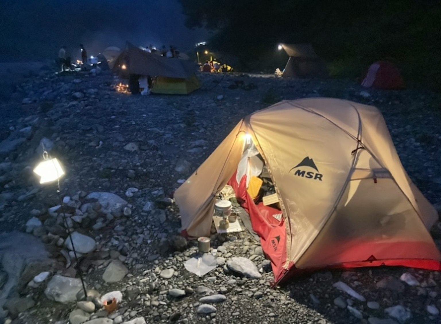 Tenda MSR illuminata sulla riva del fiume di notte