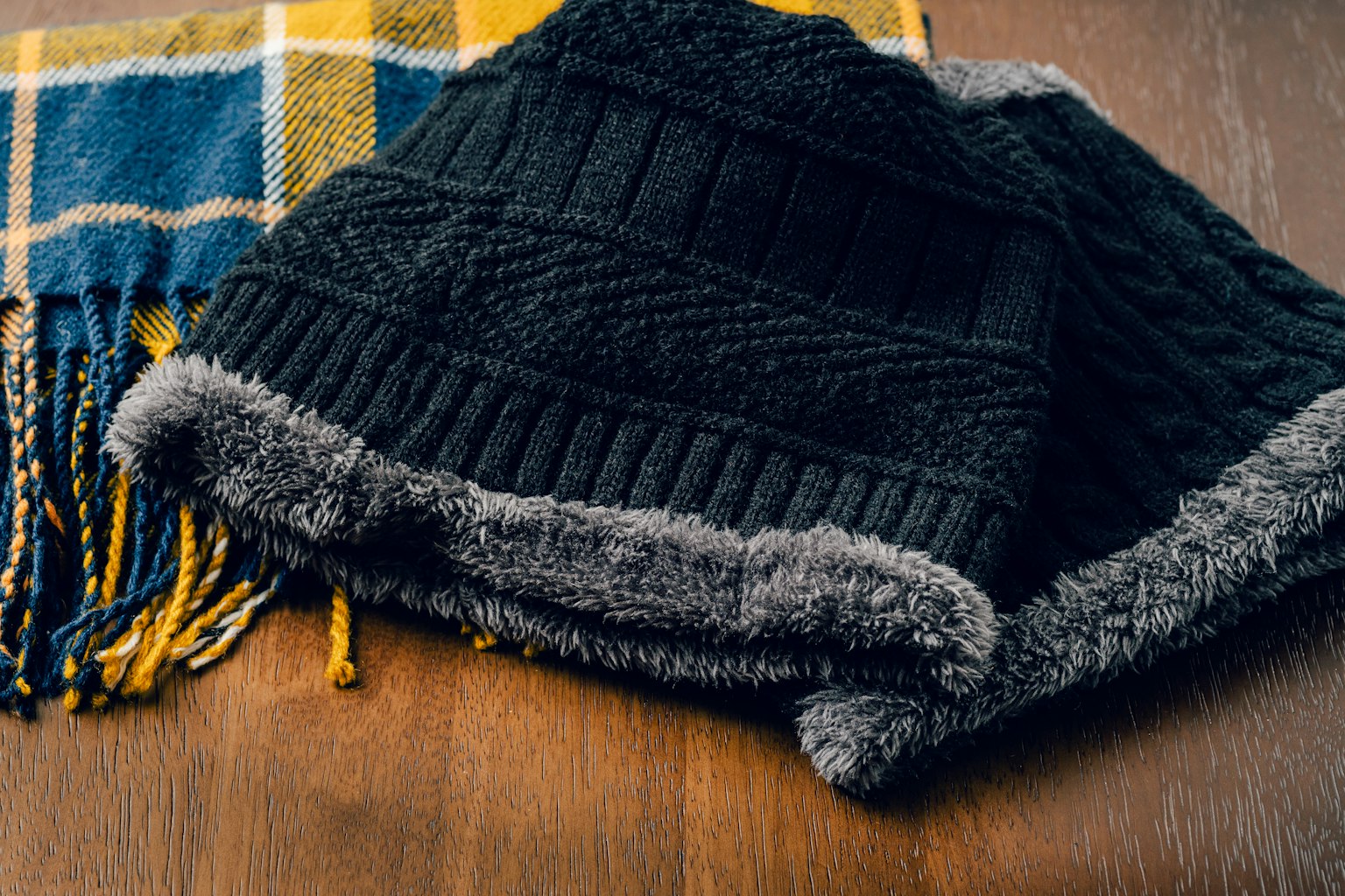 Schwarze Strickmütze und blau-gelbe karierten Schal auf einem Holztisch