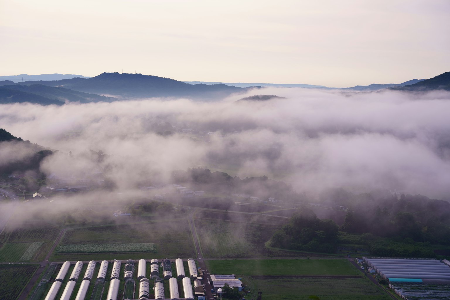 Nebeliges Landschaftsbild umgeben von Bergen mit landwirtschaftlichen Strukturen