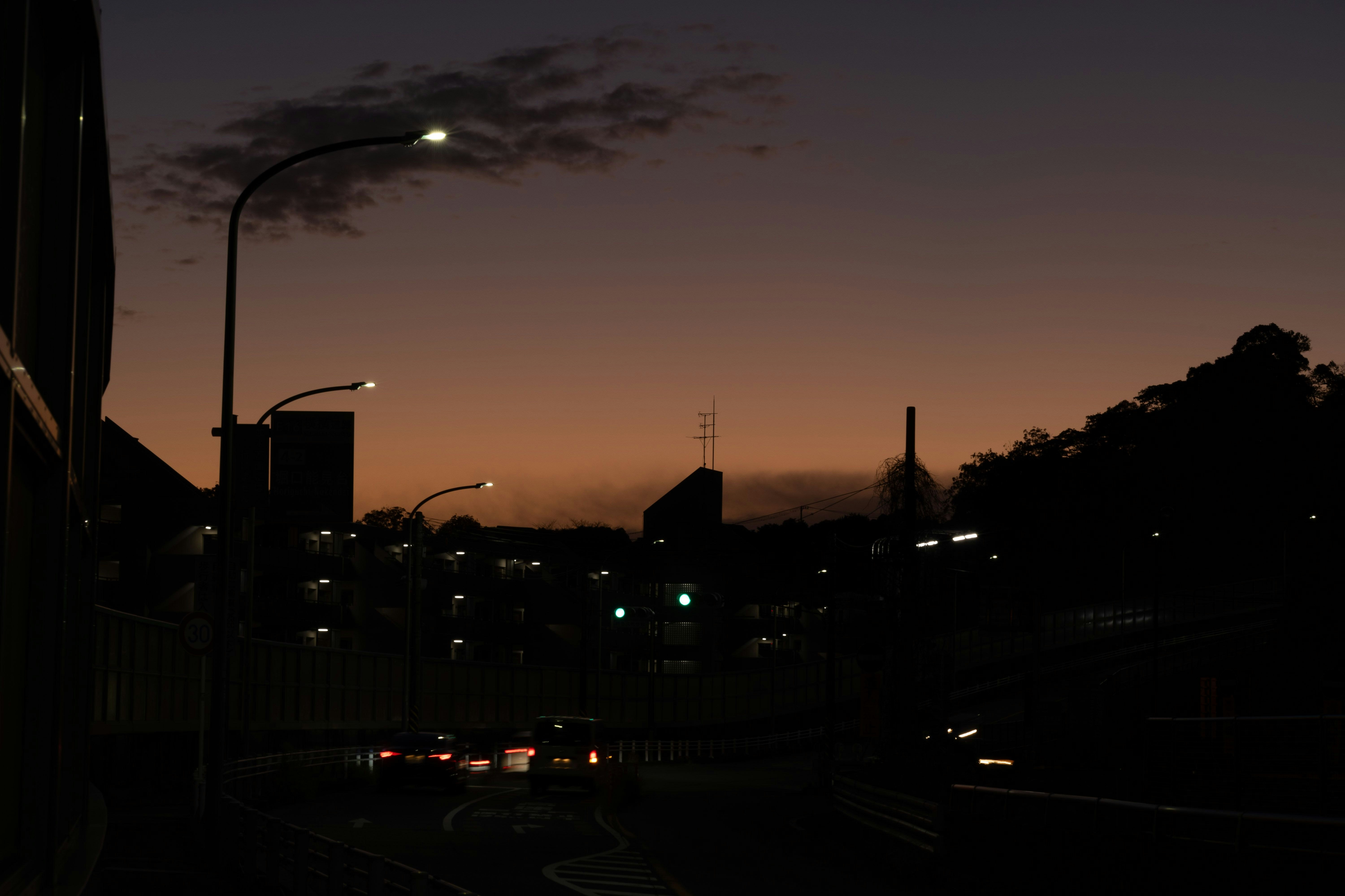 夕暮れの街道を走る車のライトがにじむ風景