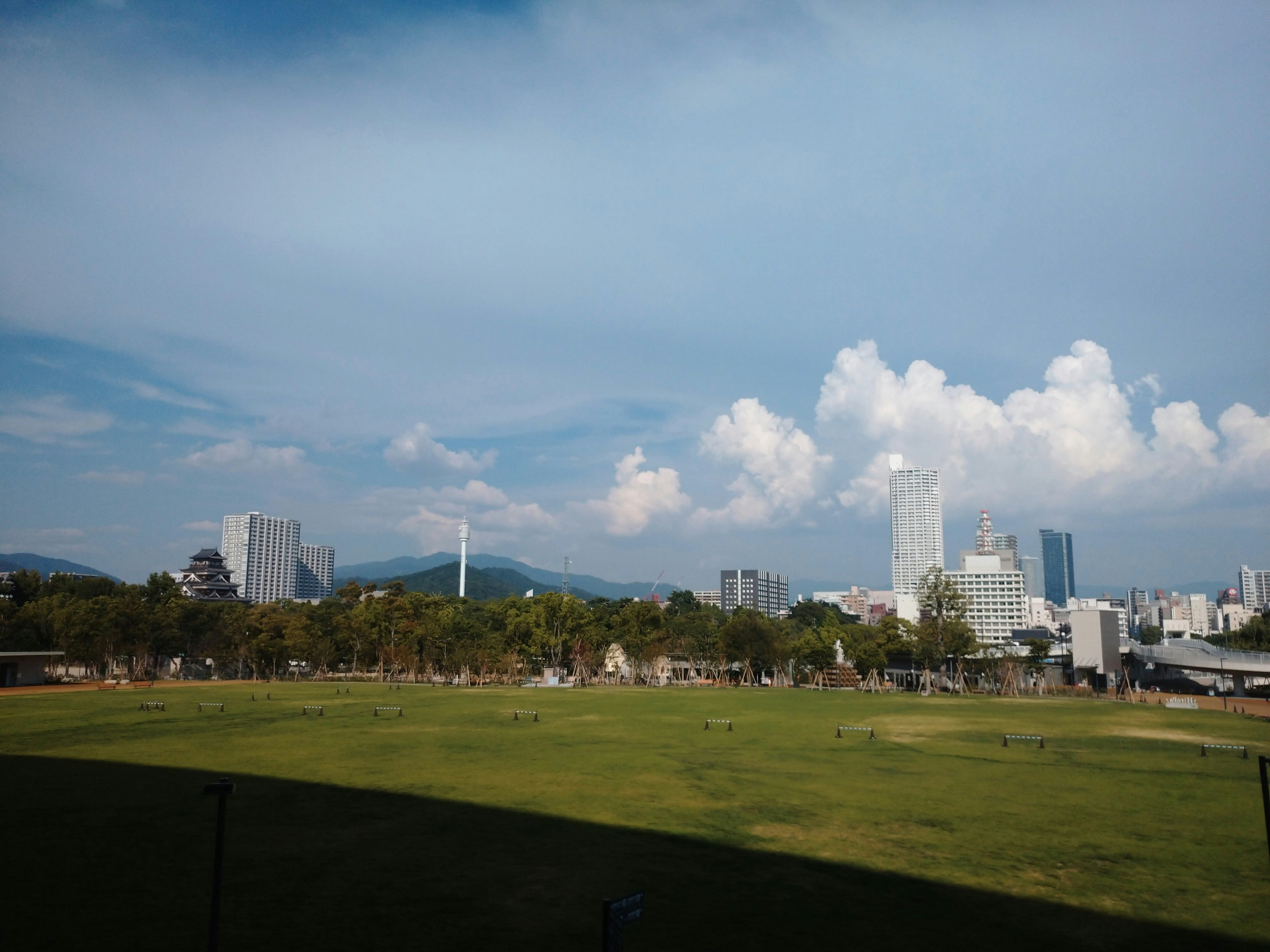 A city park scene with wide green lawn under a blue sky and clouds