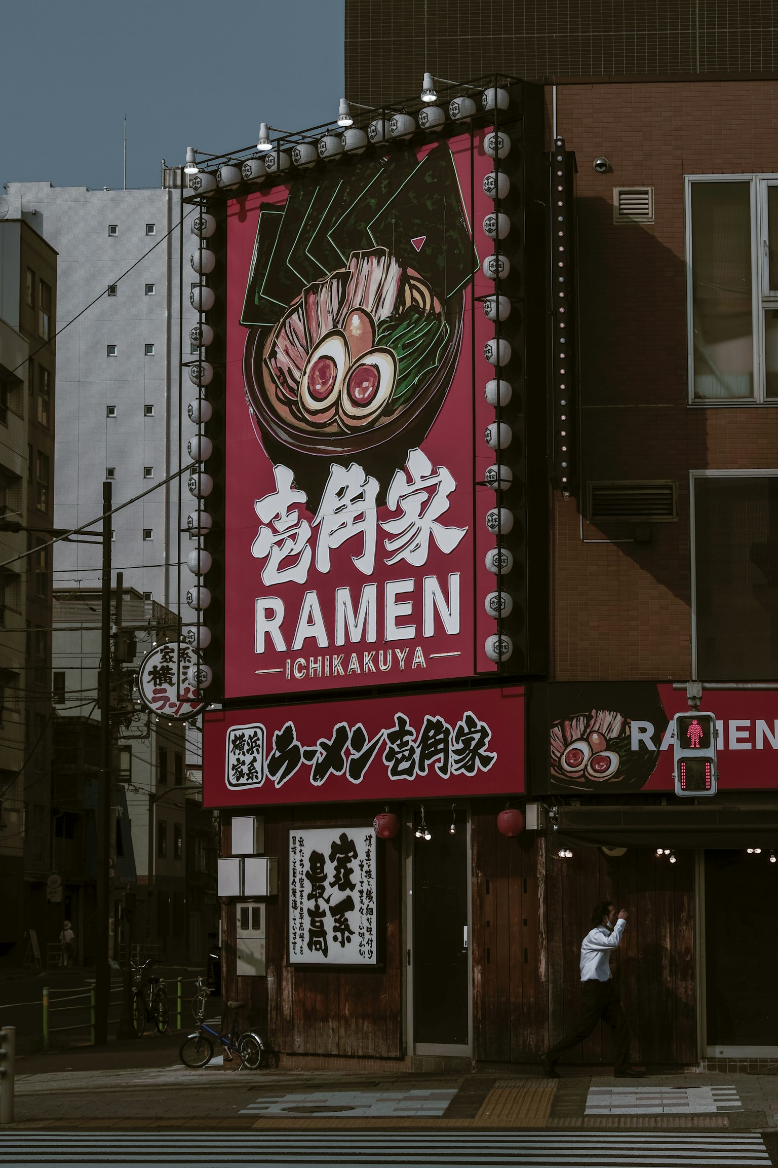 Lebendige Ramen-Shop-Schild an einer Straßenecke mit rotem Hintergrund weißem Text und Ramen-Illustration