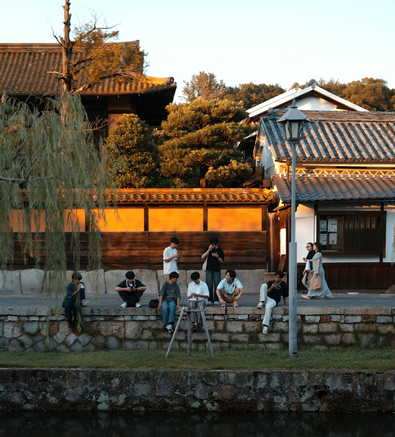 夕暮れ時の川沿いに座る人々と伝統的な建物が映る風景