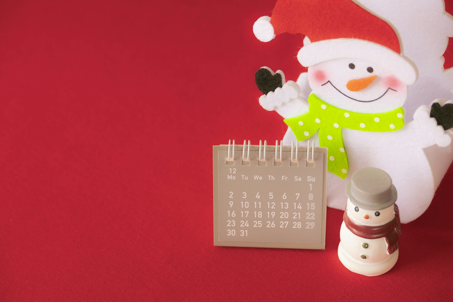 Boneka salju mengenakan topi Santa di samping kalender di latar belakang merah