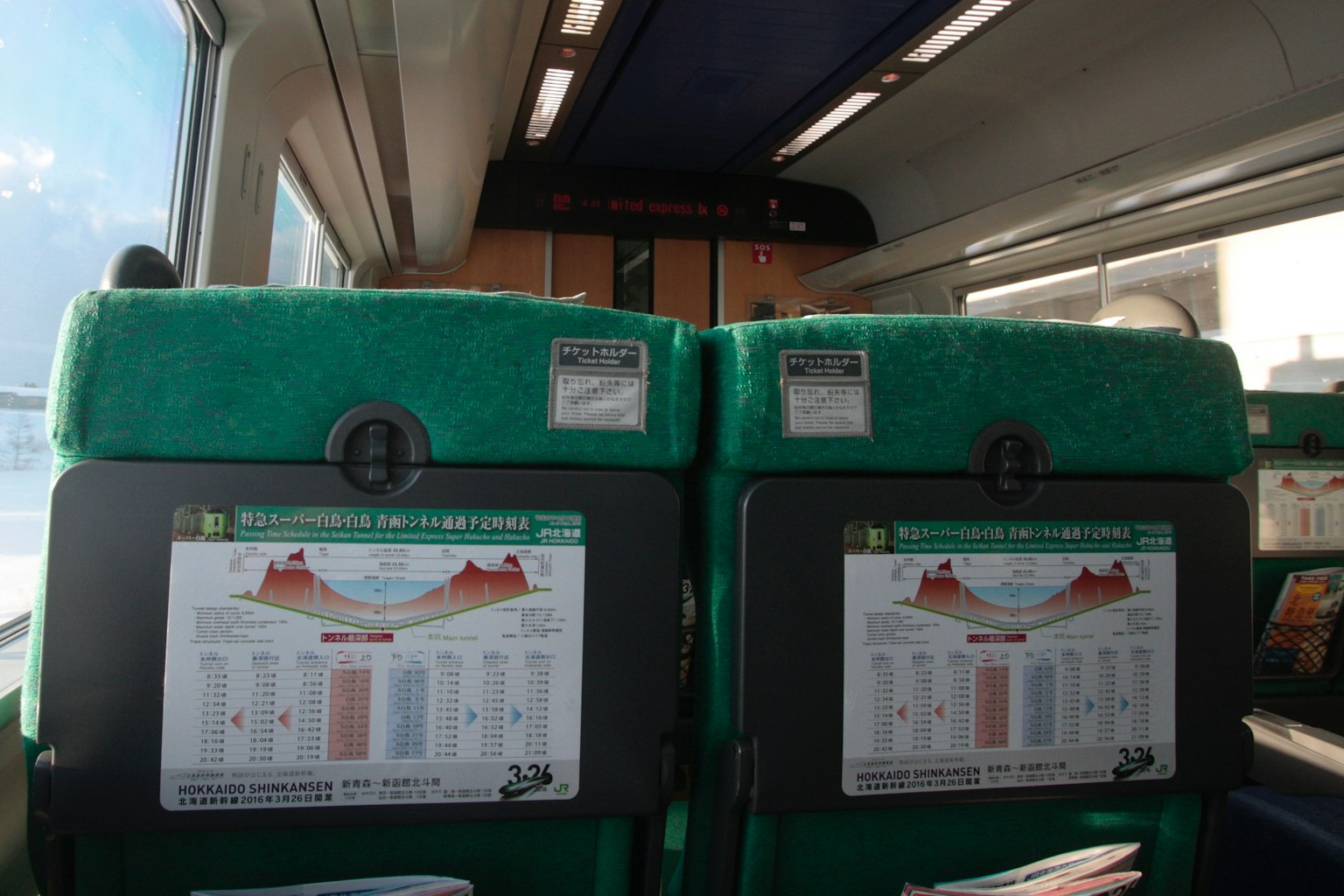 Vista interior de un tren con asientos verdes y paneles informativos en los respaldos