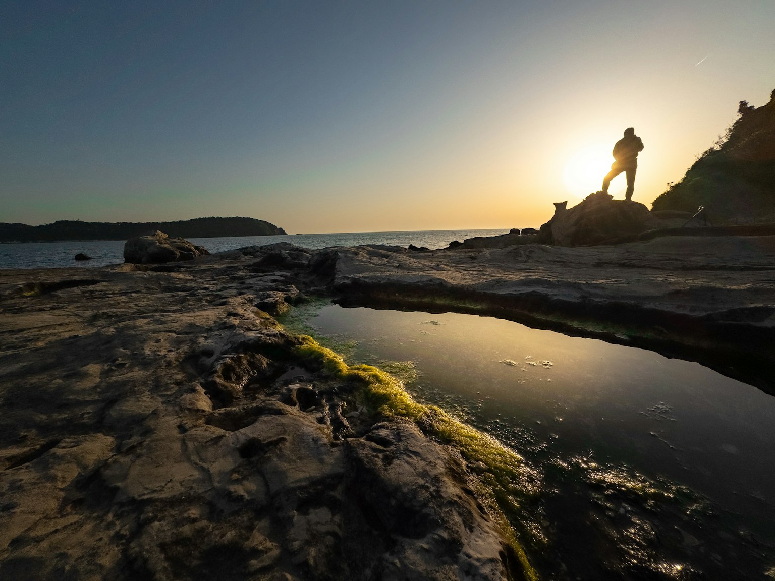日落背景下站在岩石上的人物輪廓與潮池