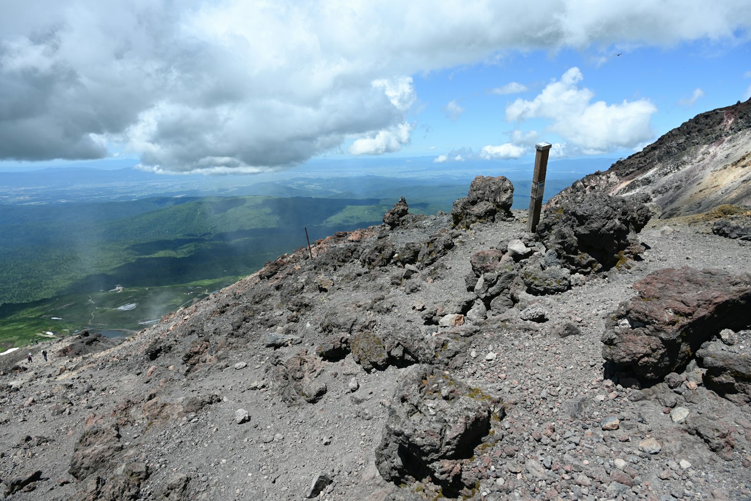 View from the summit of a volcano showing rocky terrain and a blue sky with clouds