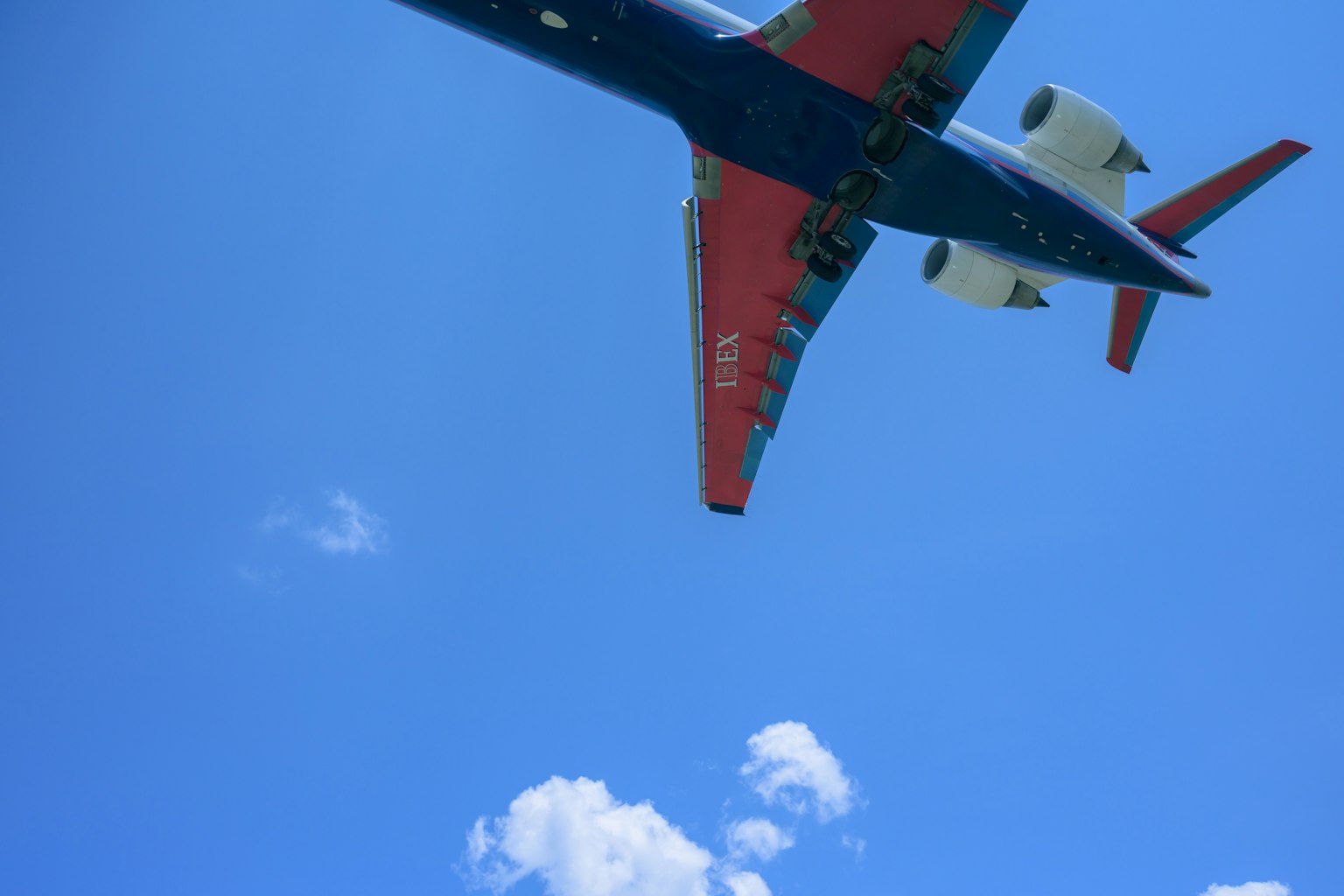 Sebuah pesawat merah dan biru terbang di latar belakang langit biru yang cerah