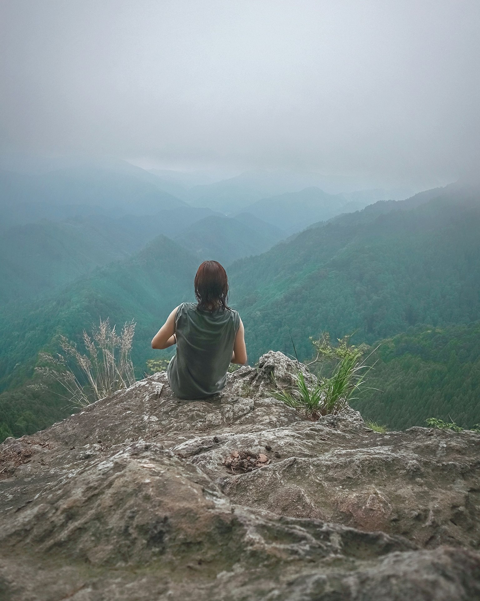 Người phụ nữ ngồi trên đỉnh núi nhìn ra những ngọn đồi và thung lũng mờ sương
