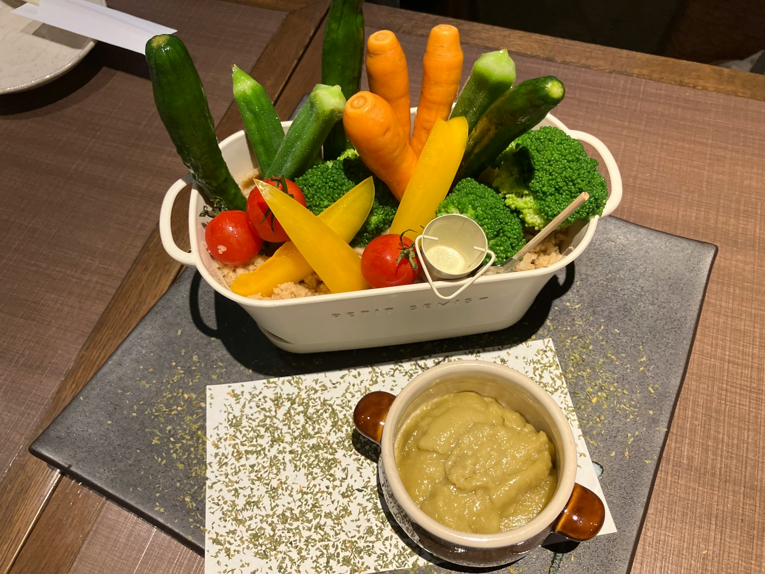 Un plateau de légumes colorés comprenant des courgettes des carottes et du brocoli servi avec une sauce