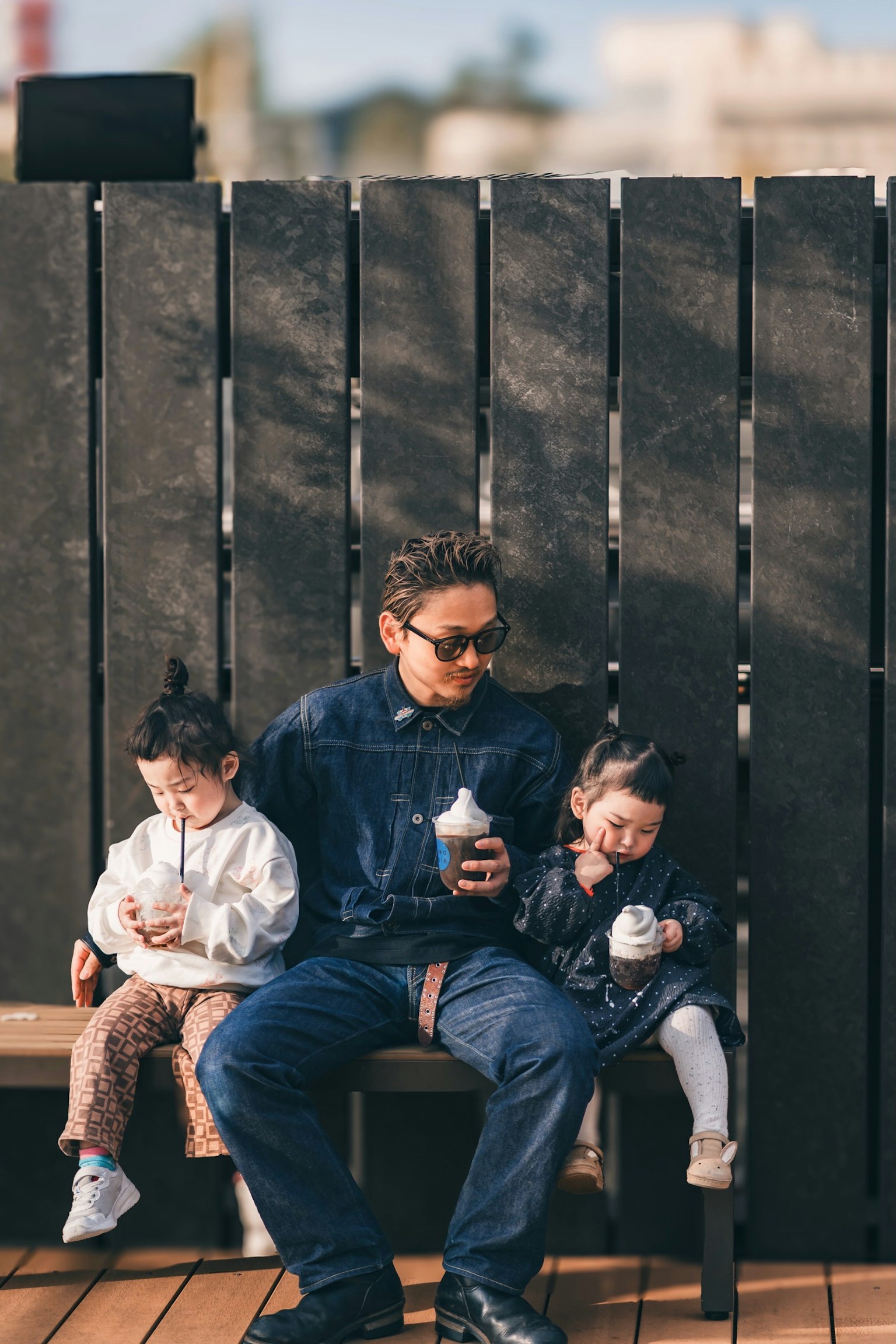 父親と二人の子供がベンチに座っているシーン 子供たちは飲み物を持っている