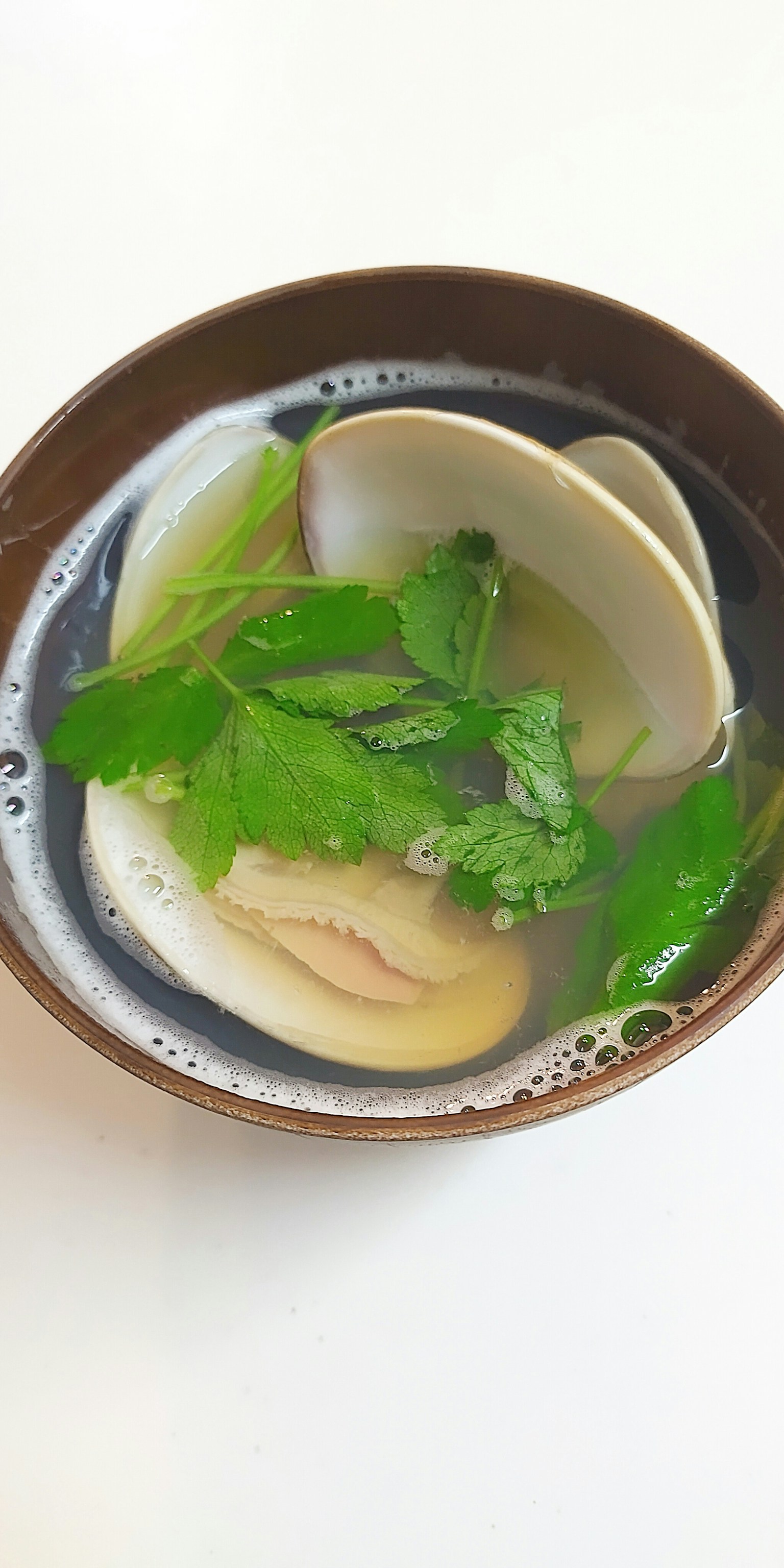 Braune Schüssel mit Muschelsuppe und Kräutern