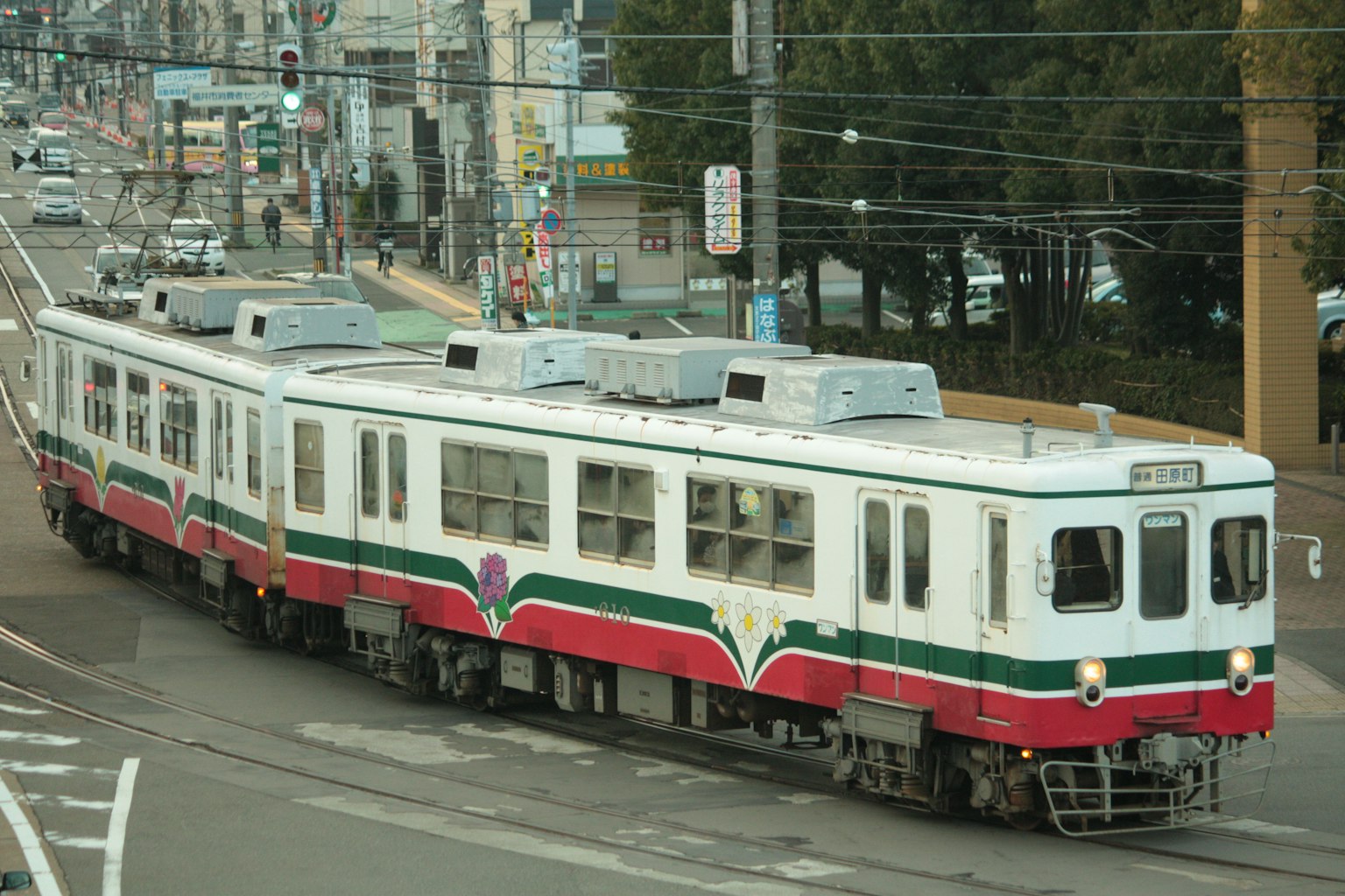 Train with red and green stripes traveling through the city
