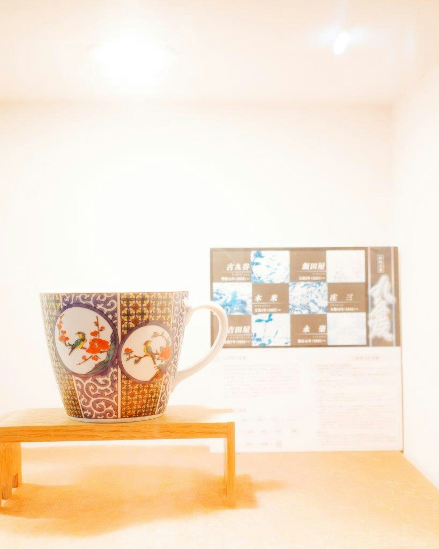 一只精美设计的杯子放置在木桌上，背景是白色的墙壁和艺术作品