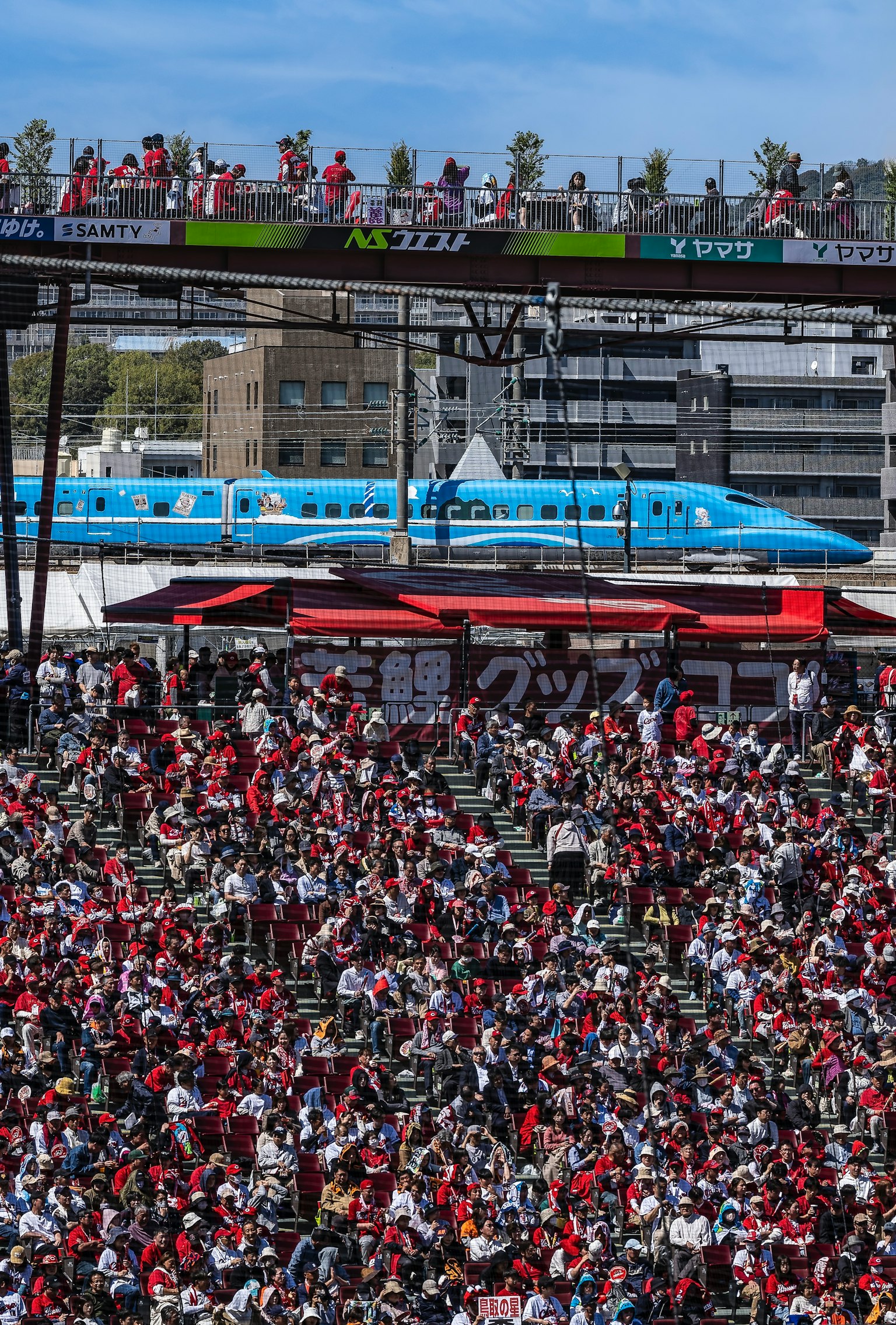 Uno stadio affollato con fan in rosso e un treno blu che passa sopra