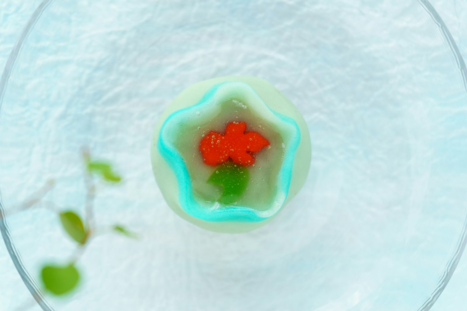 Blütenförmiges Dessert mit blauen Rändern, belegt mit roten Früchten und grünen Blättern