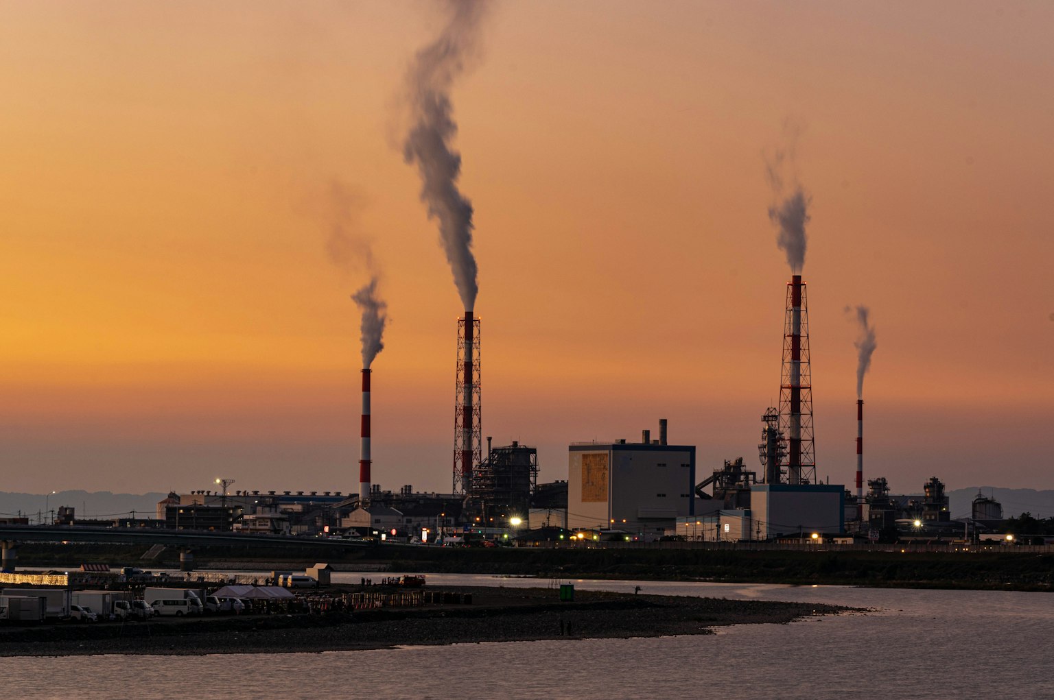 Silhouette einer Fabrik, die Rauch gegen einen Sonnenuntergangshimmel ausstößt